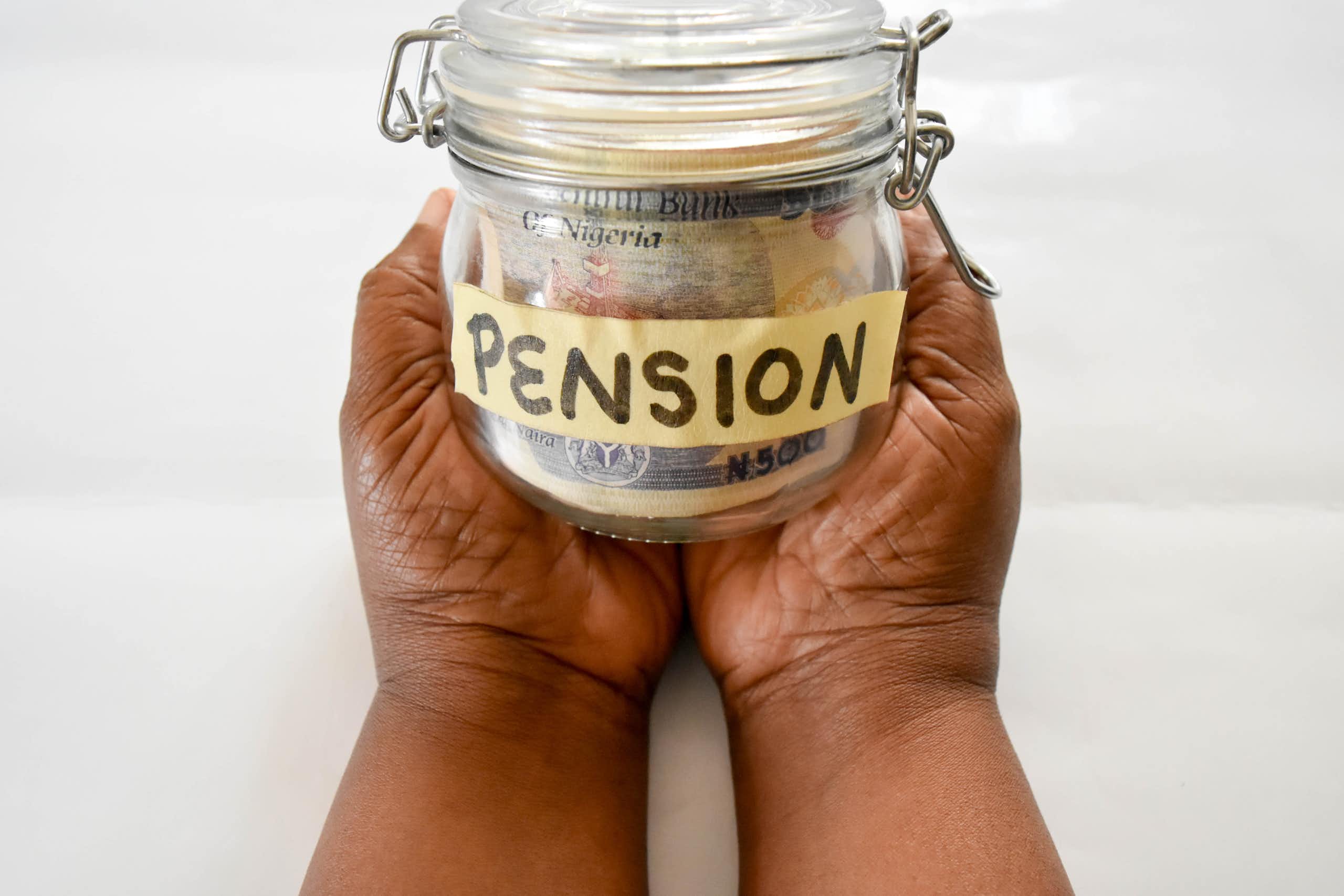 A photograph of a pair of hands holding Nigerian banknotes in a small bottle.