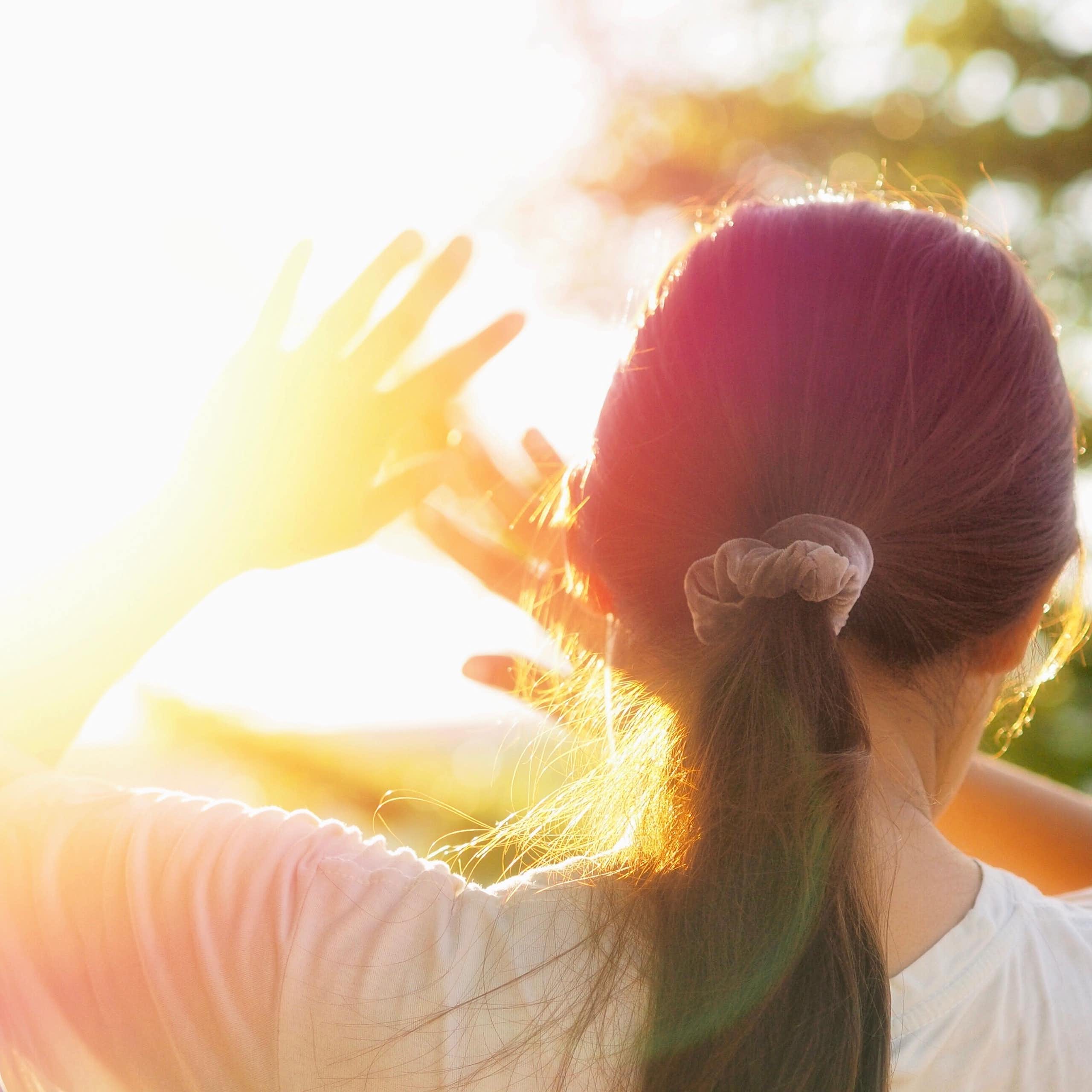Une jeune fille se protège du Soleil, mains levées