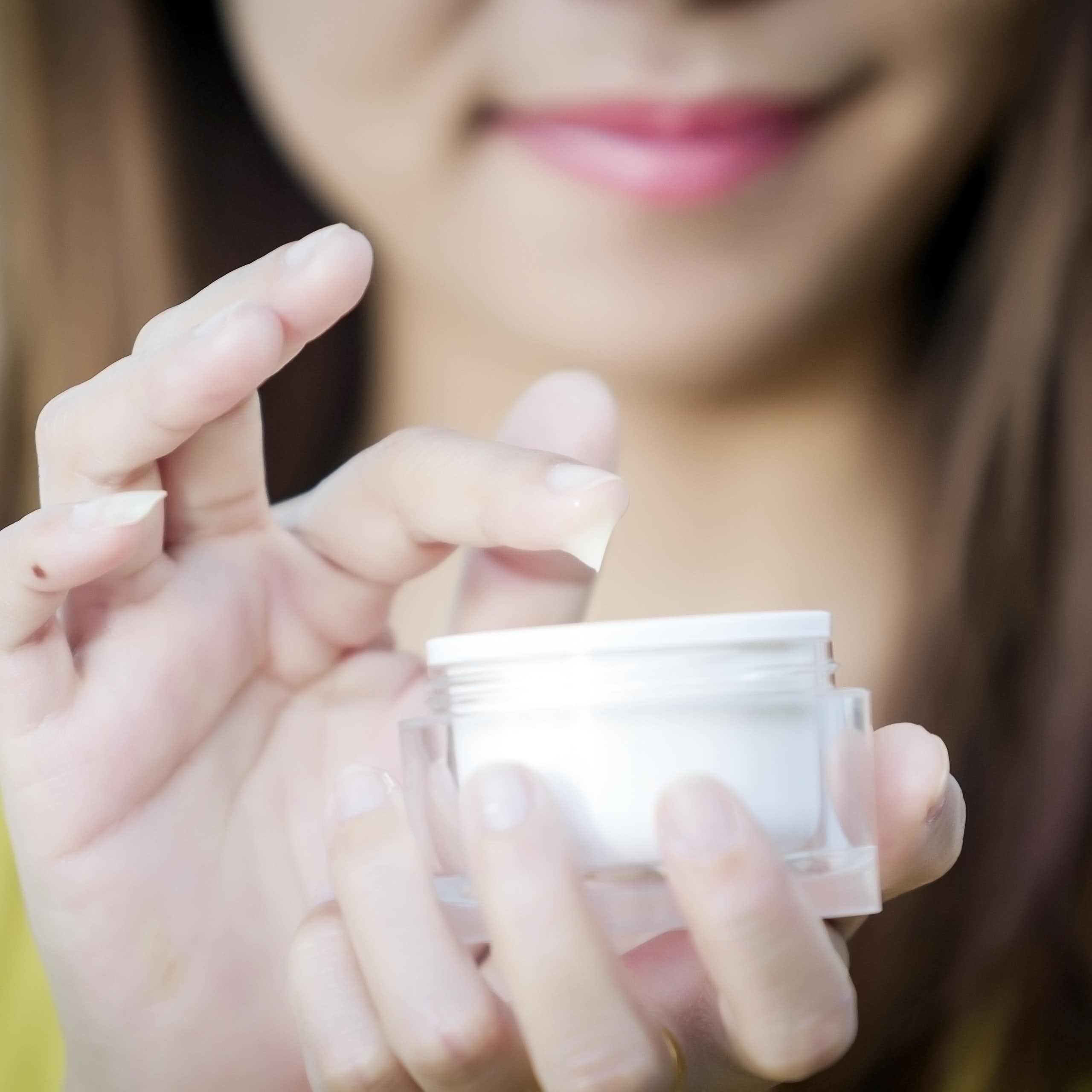 Une femme trempe son doigt dans une crème pour le visage.