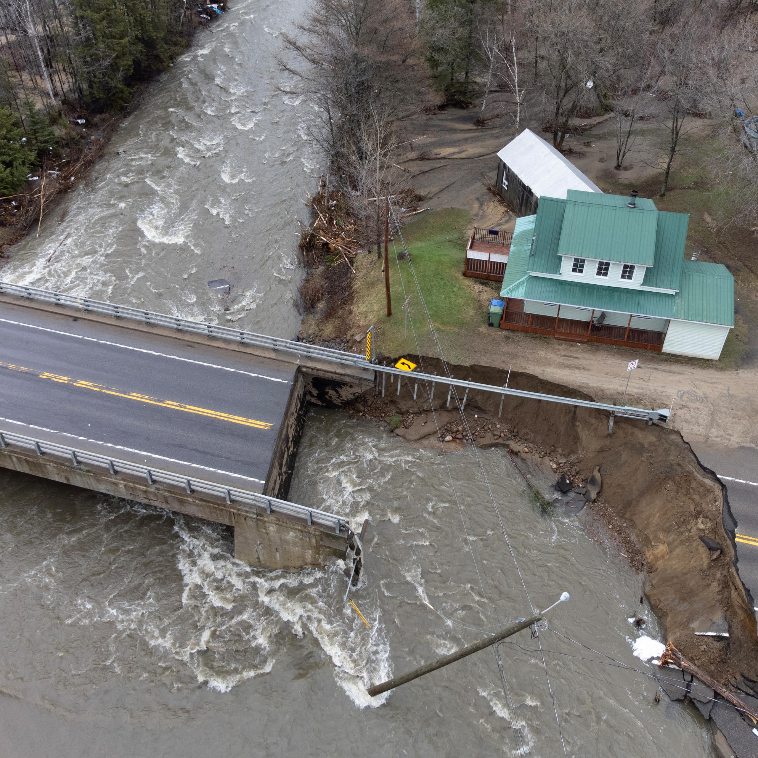 Vue aérienne d'une zone inondée, avec une route coupée en deux, et une maison au toit vert en arrière-plan