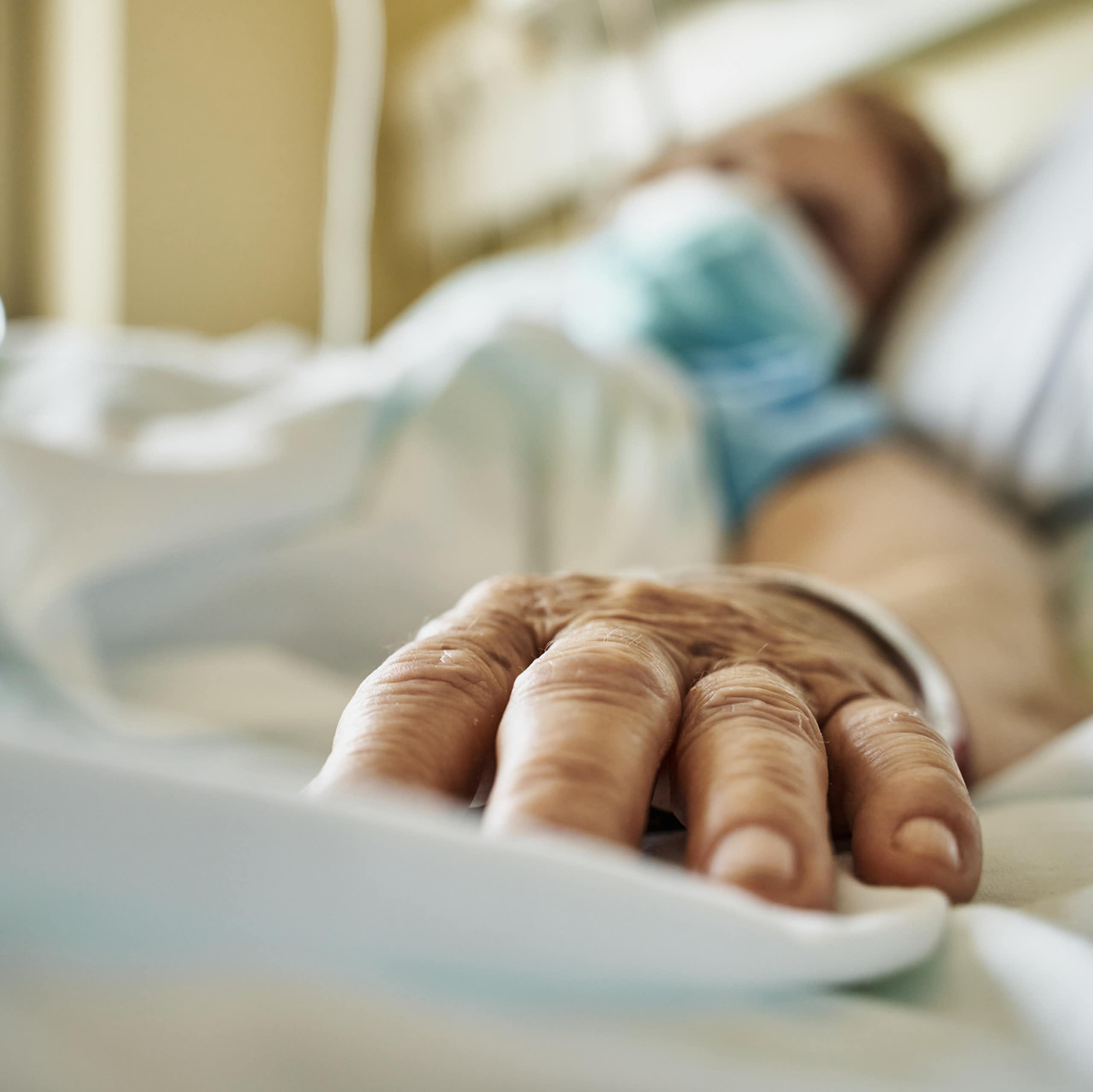 Patient portant un masque, allongé sur un lit d'hôpital, main tendue vers la caméra