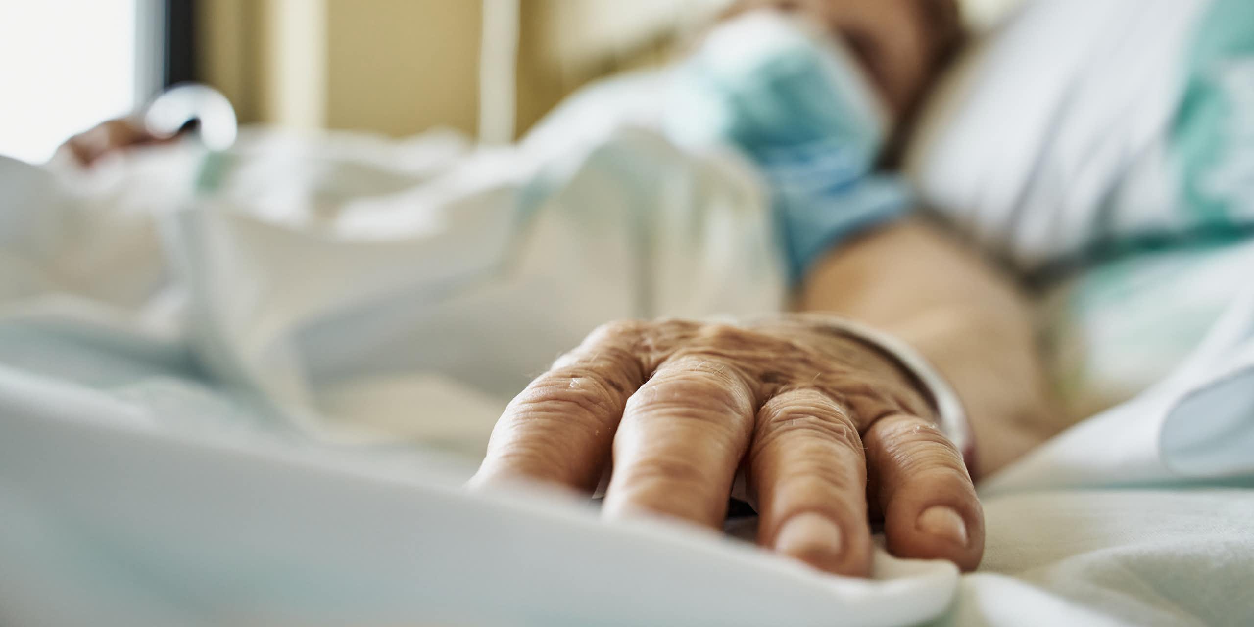 Patient portant un masque, allongé sur un lit d'hôpital, main tendue vers la caméra