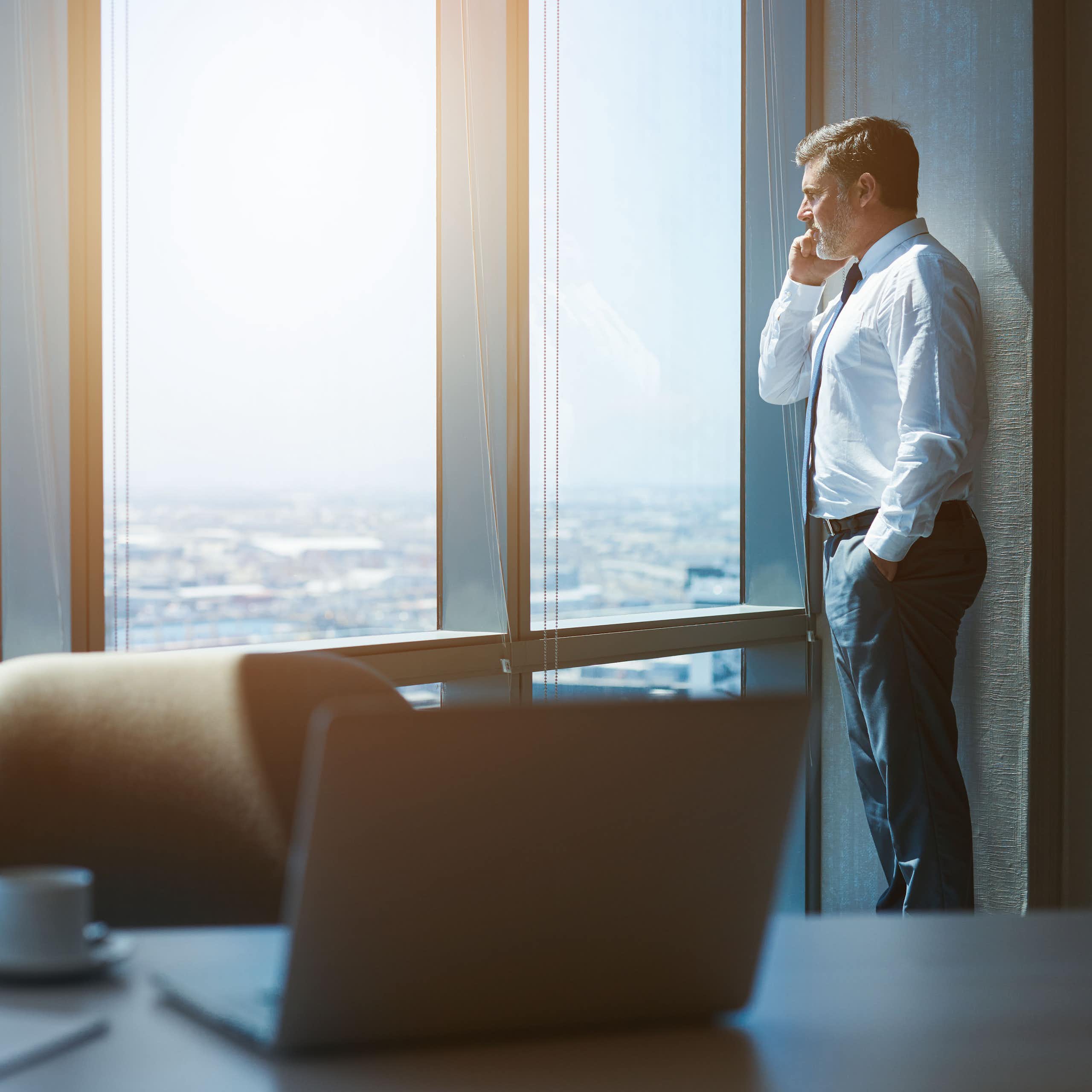 Standing man looking out window while on his cell phone