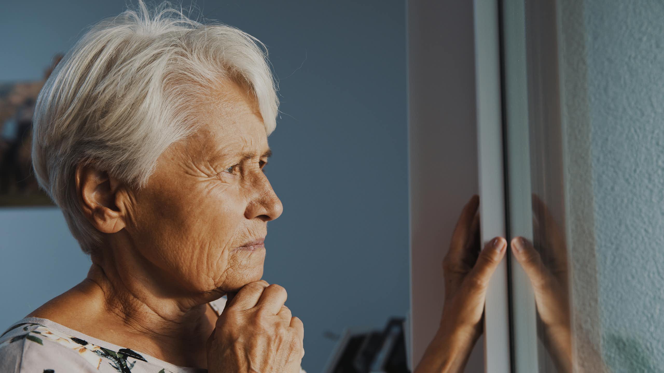 Une aînée regarde par la fenêtre d'un air préoccupé