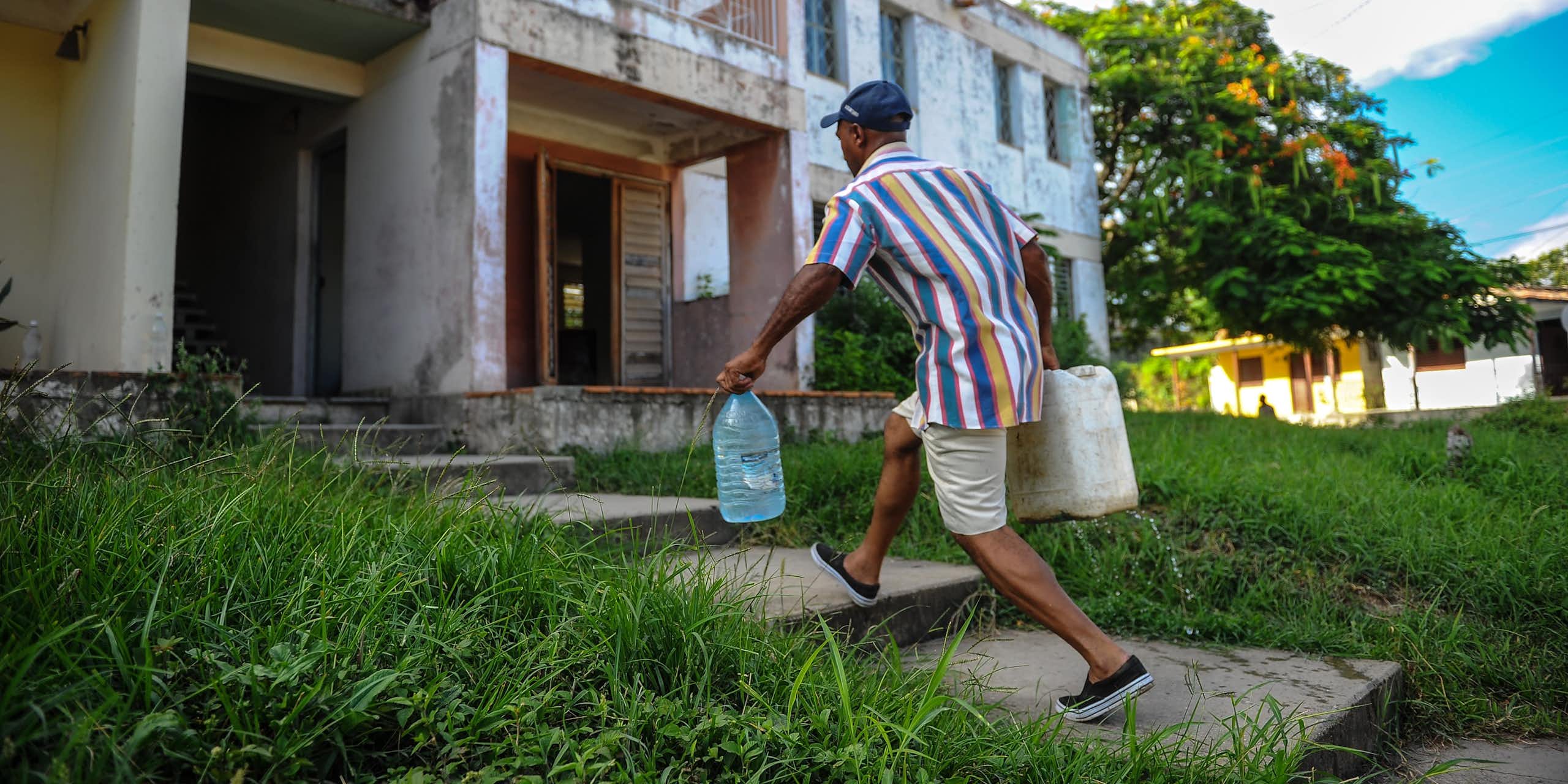 A man carries two large jugs of water to an apartment building.