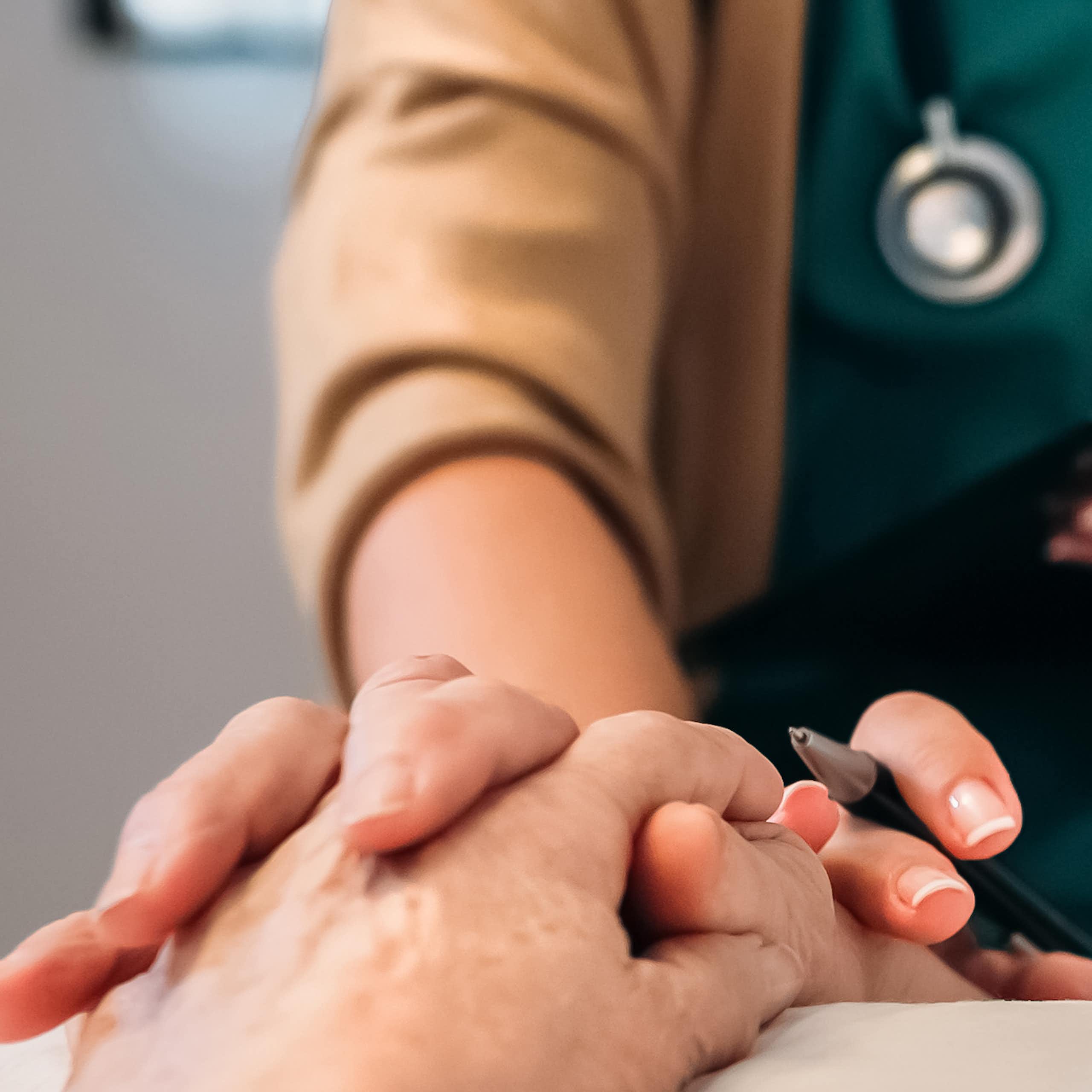 A doctor with a clipboard holds the hand of a patient on a bed.
