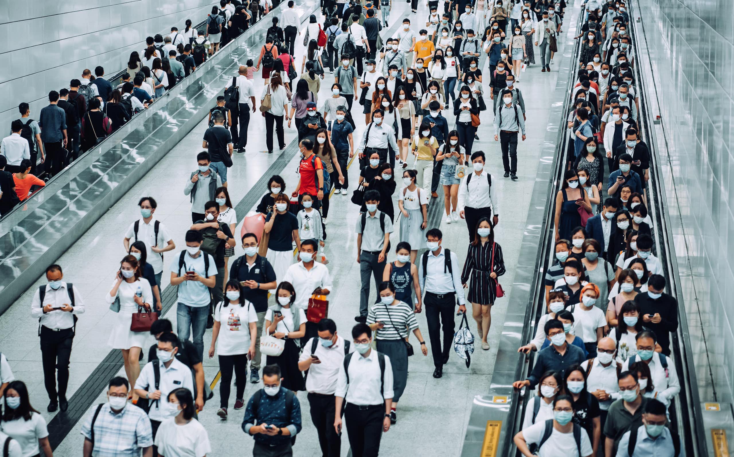 Crowd of busy commuters with face masks walking through platforms at a subway station