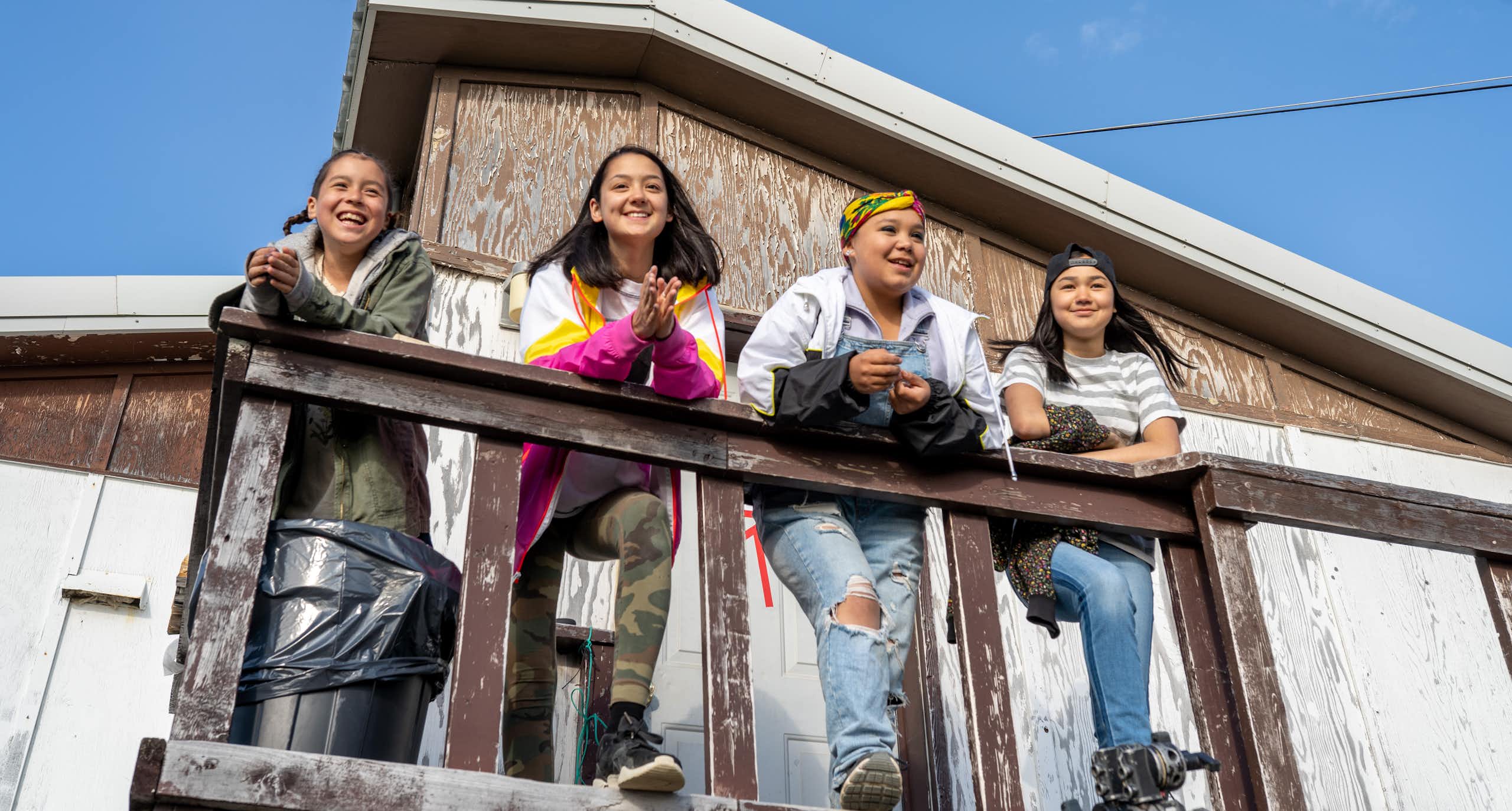 Girls standing on a porch surveying space and smiling. 