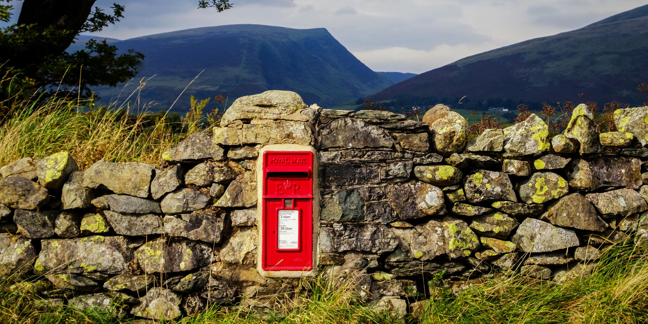 Post box in stone wall with rural backdrop.