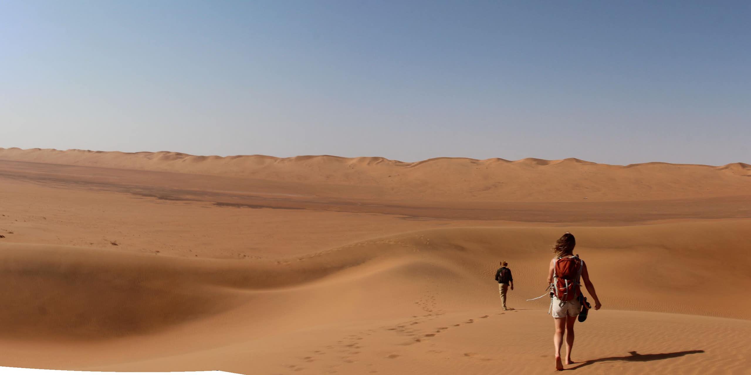 Two people walking in a landscape of sand dunes