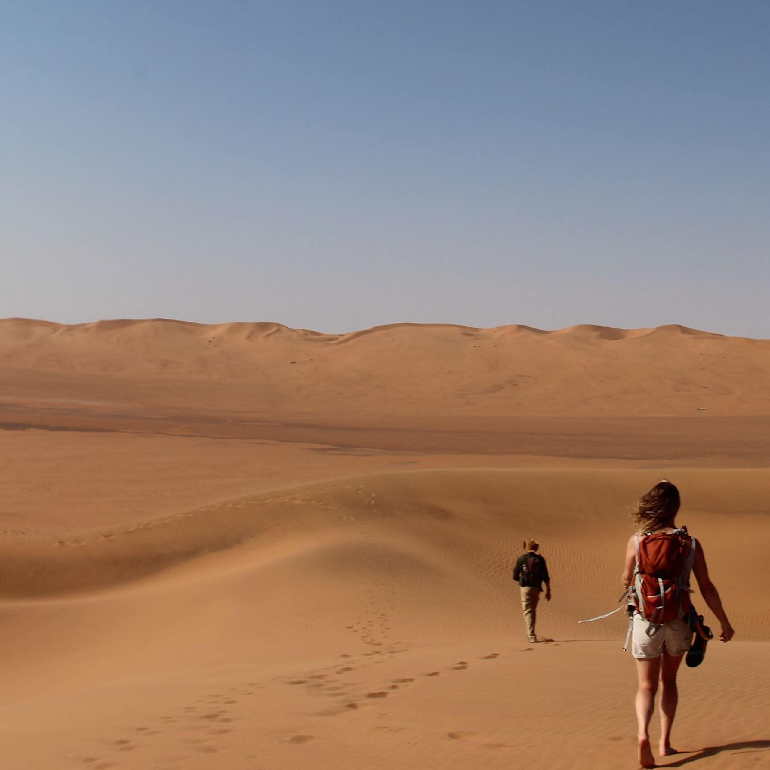 Two people walking in a landscape of sand dunes