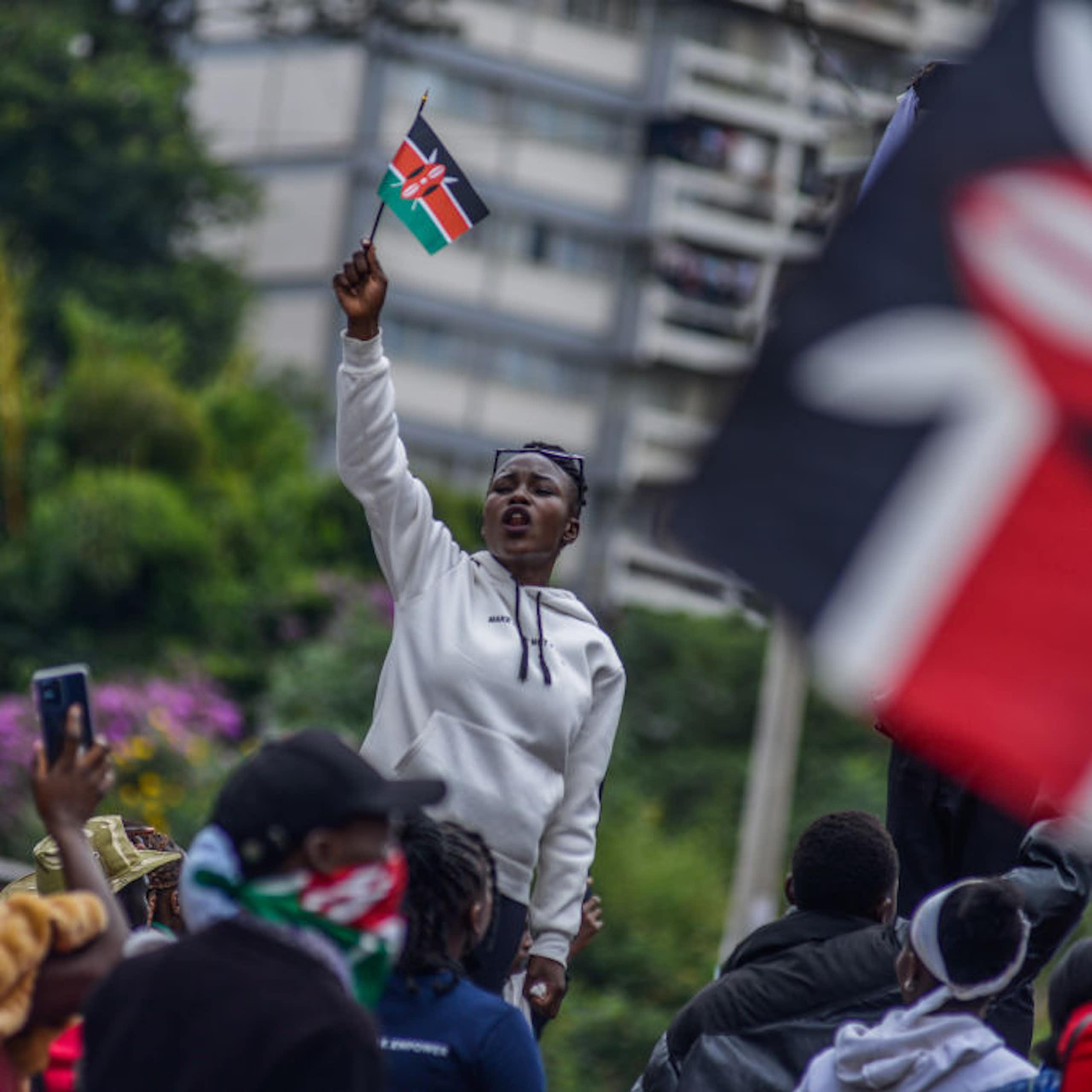 A woman in a grey jumper holding up a small flag with black, white, red and green stripes while facing a crowd of people who are also holding flags