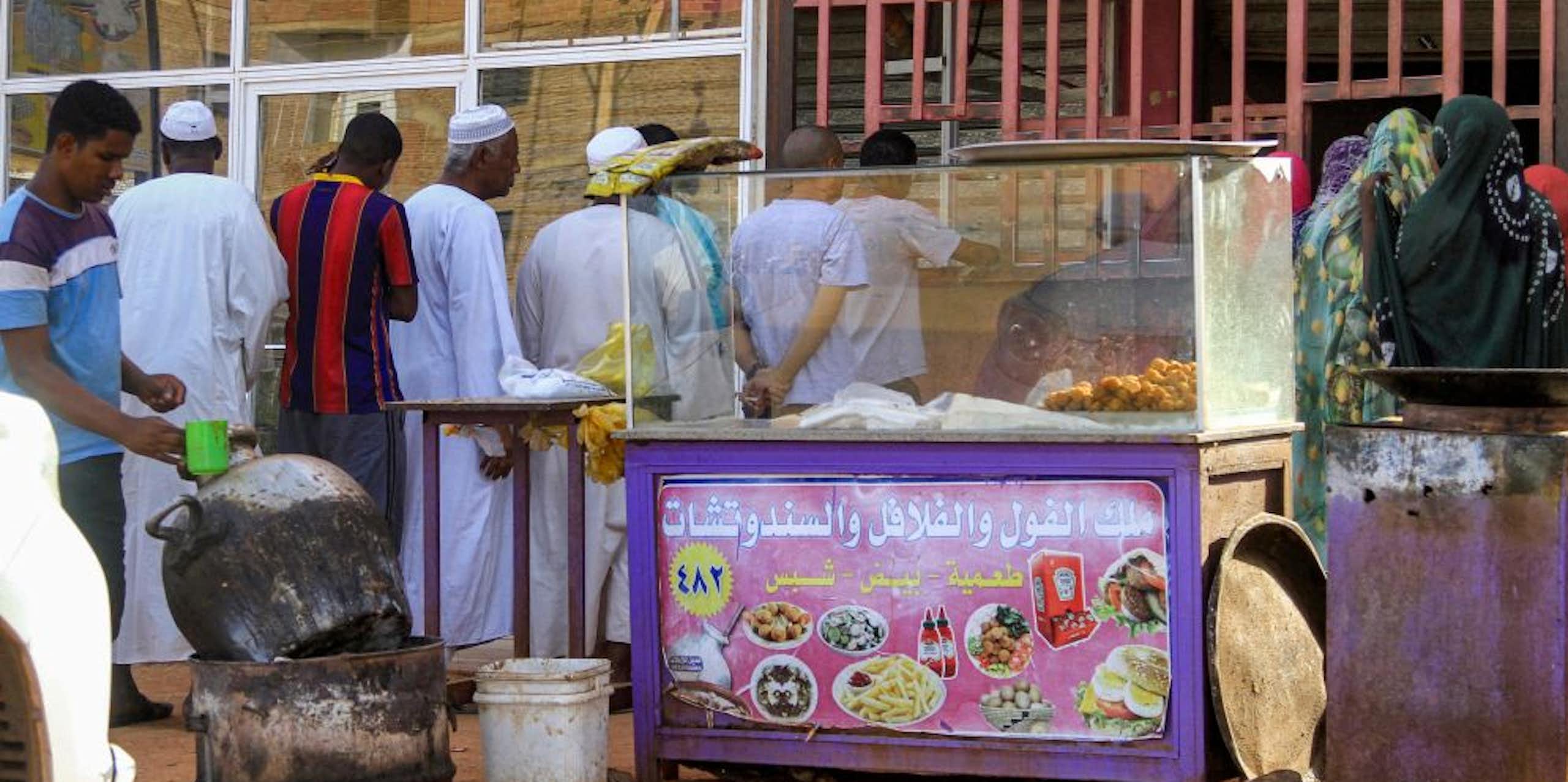 A queue forms in front of a metal grille shop window