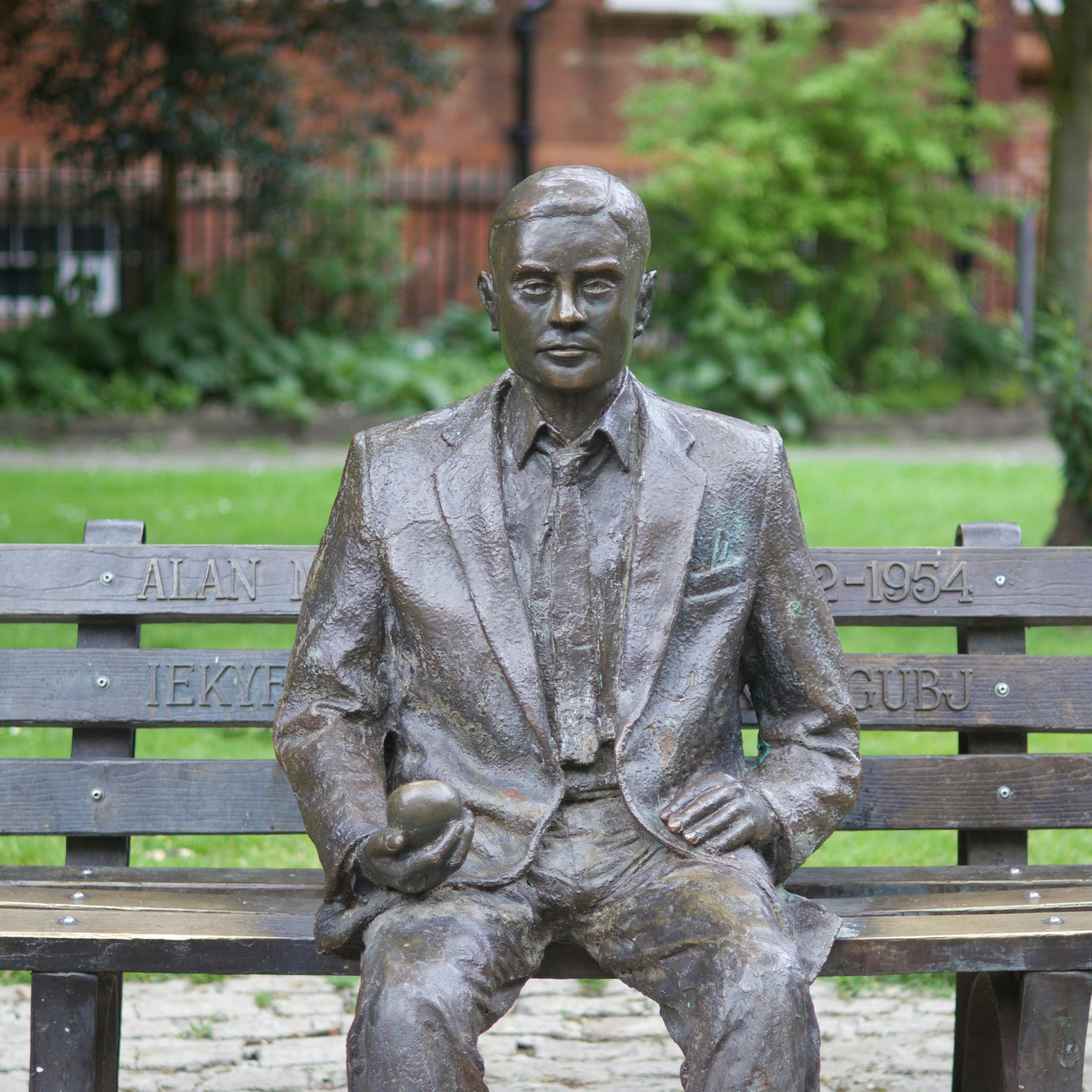 Statue d'Alan Turing assis sur un banc, une pomme dans la main, à Manchester.