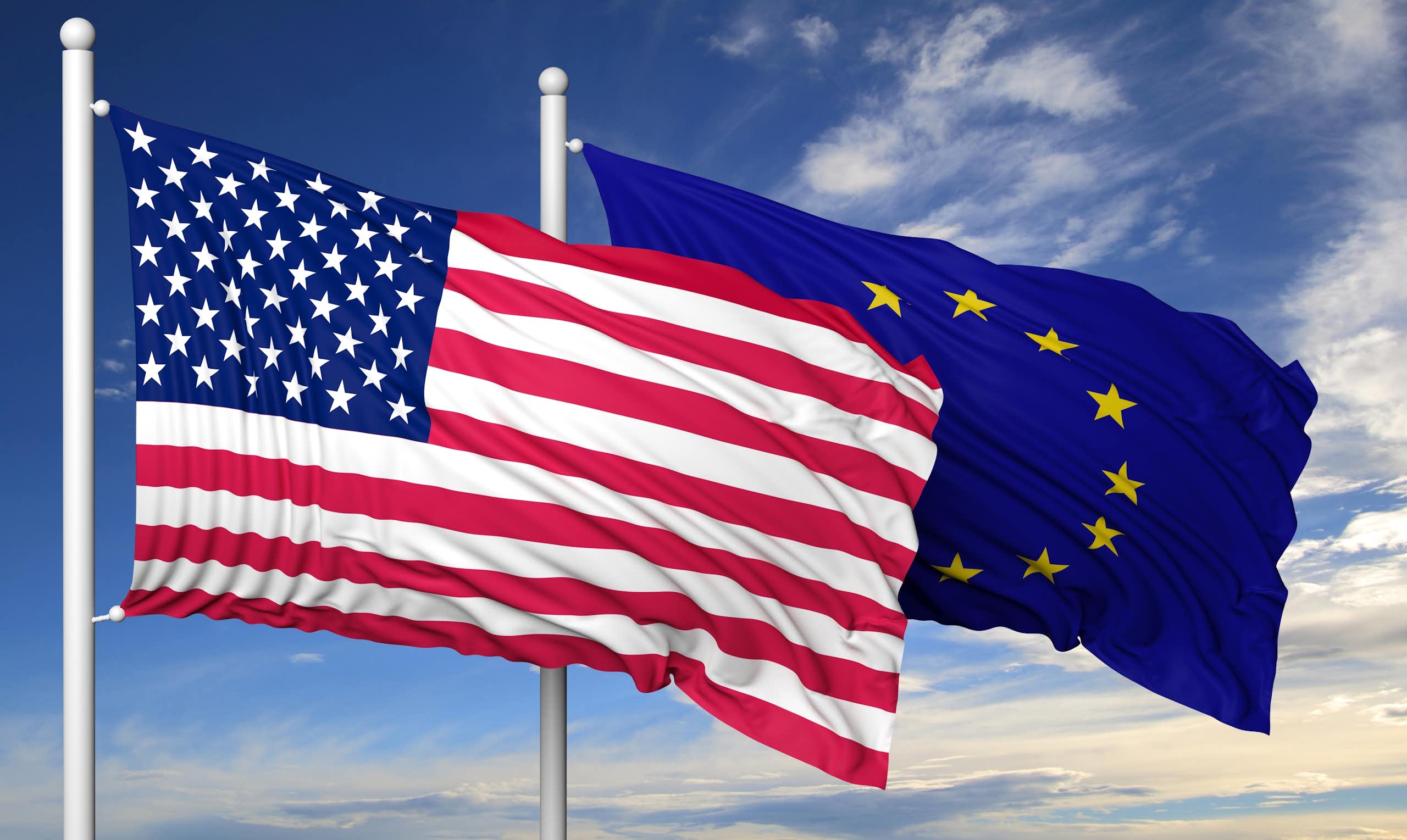 les drapeaux des USA et de l'Union européenne flottent sur un ciel bleu. 
