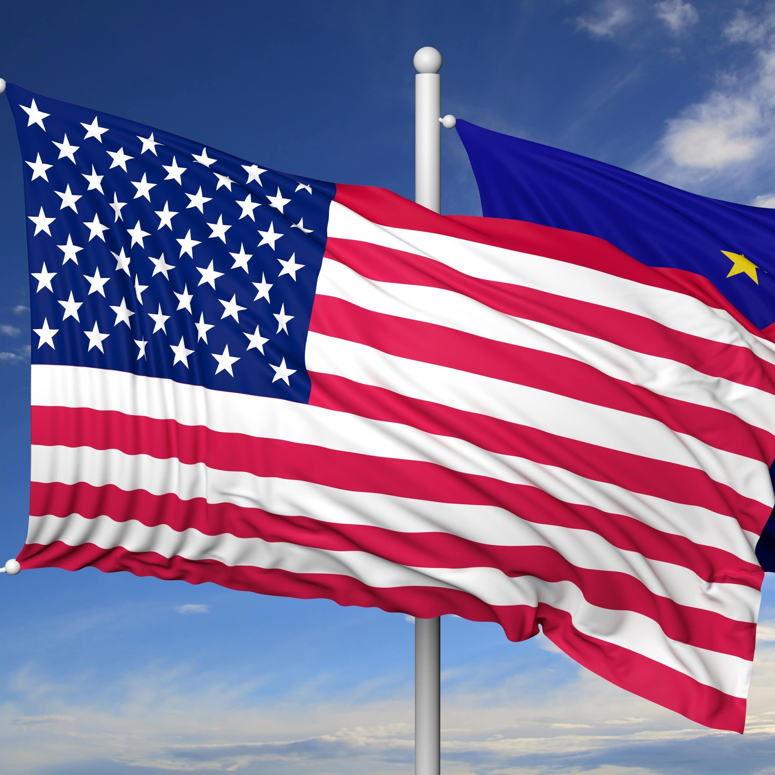 les drapeaux des USA et de l'Union européenne flottent sur un ciel bleu. 