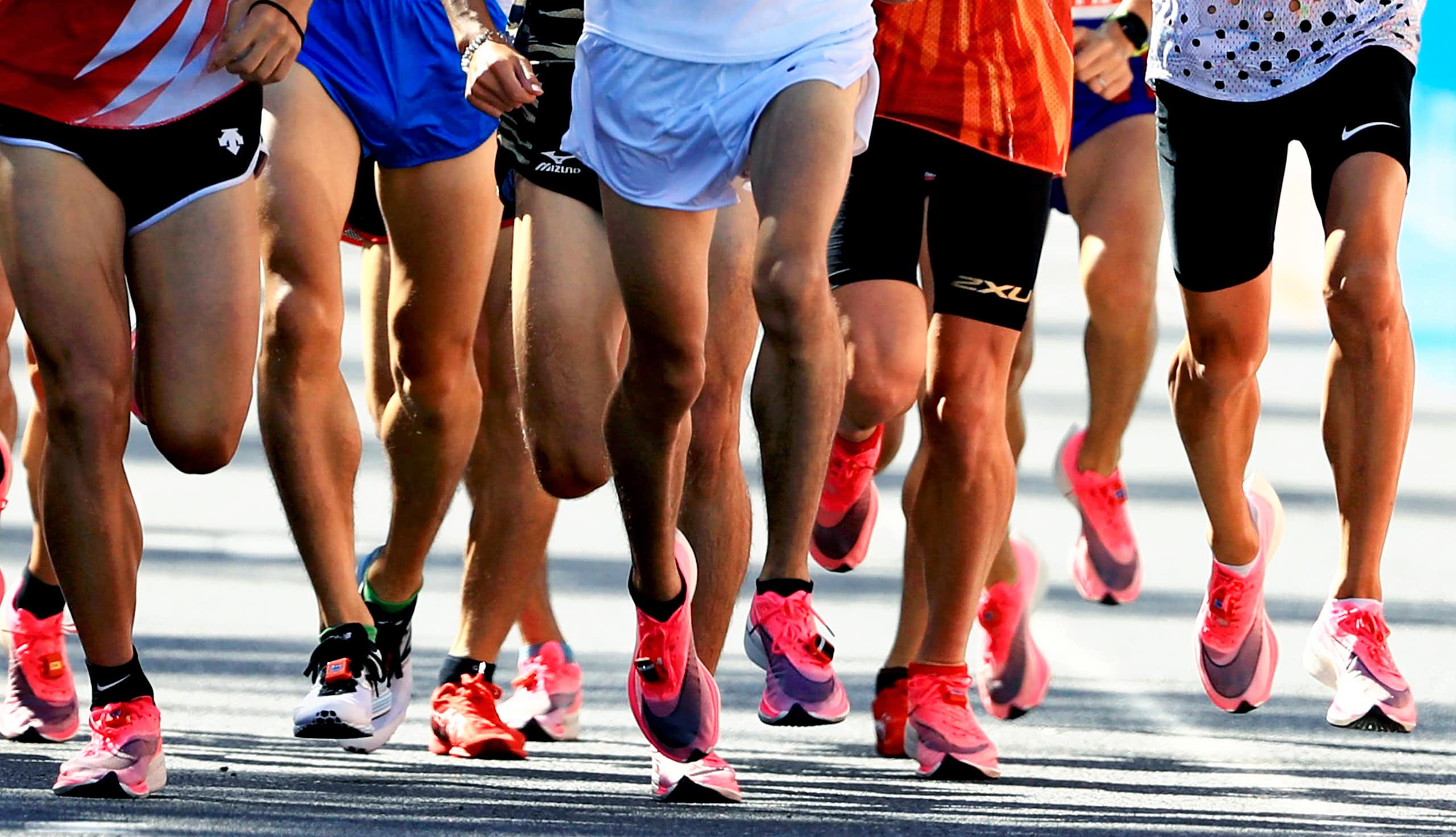Action shot of a large group of people running, most wearing white and pink Nike shoes.