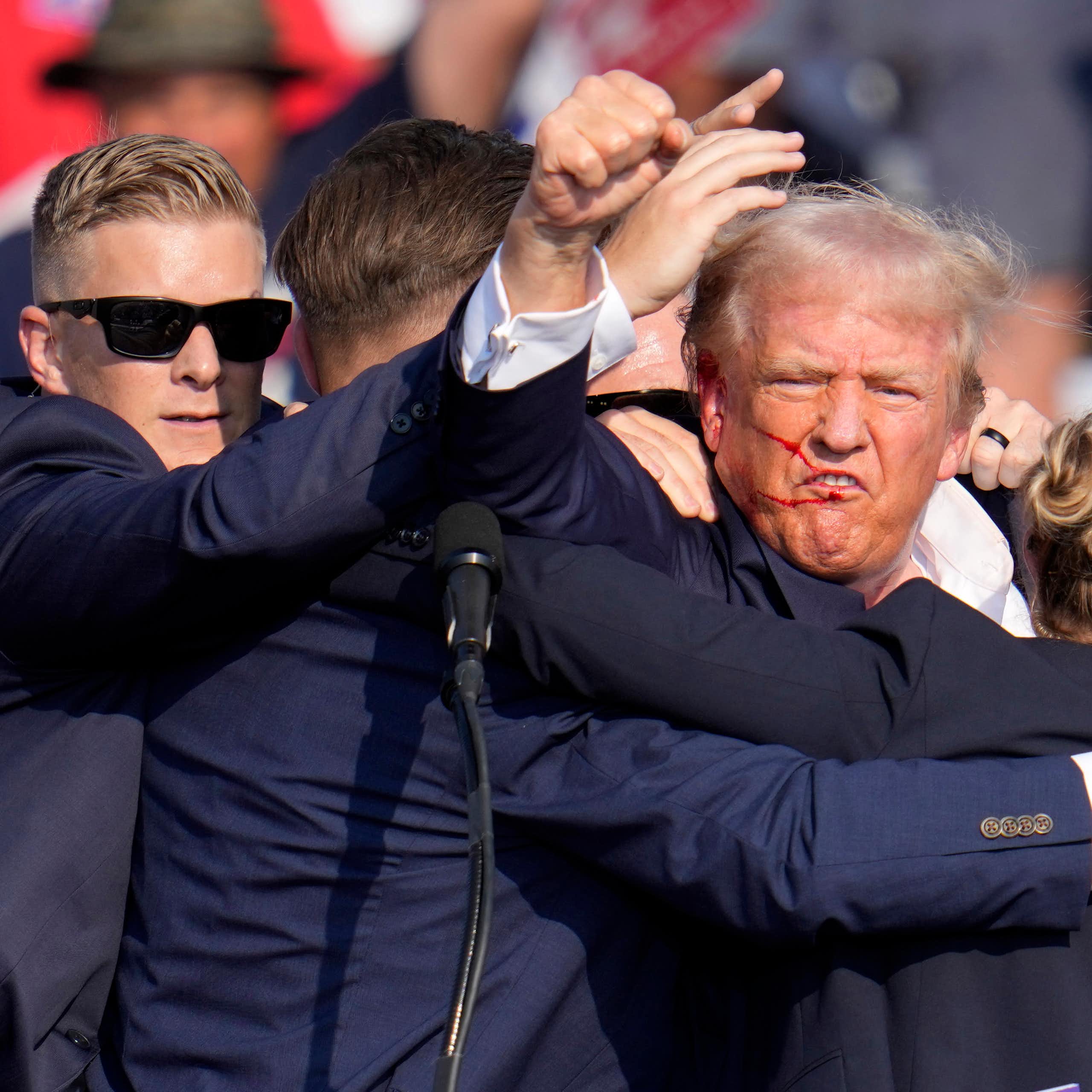 A man in a dark blue jacket, being pulled by several others, raises his fist.