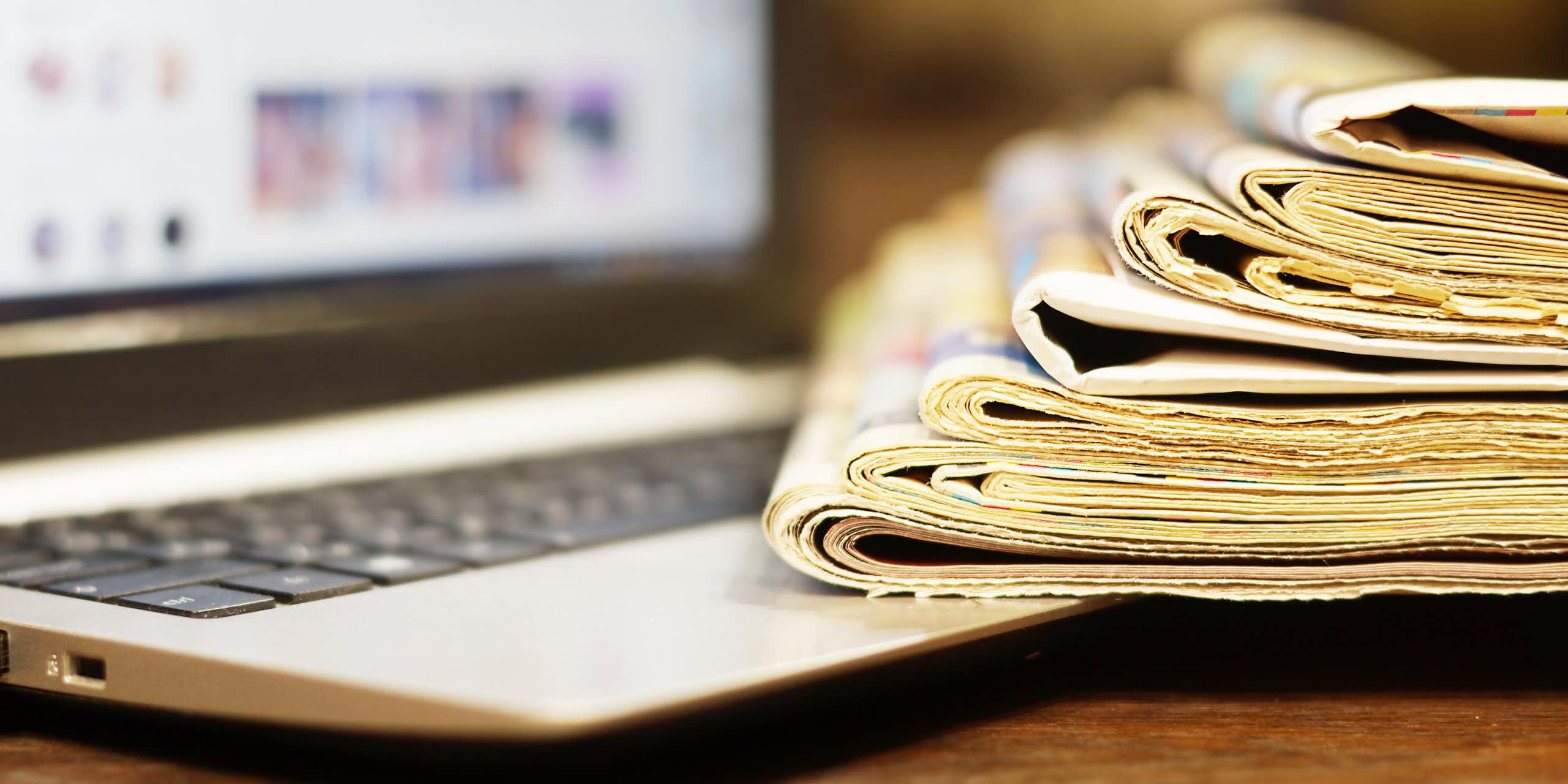 A stack of newspapers beside a laptop