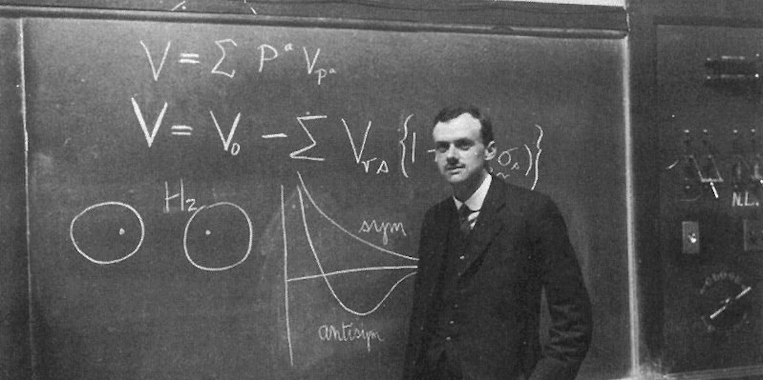 Portrait de Paul Dirac en noir et blanc, devant un tableau noir.