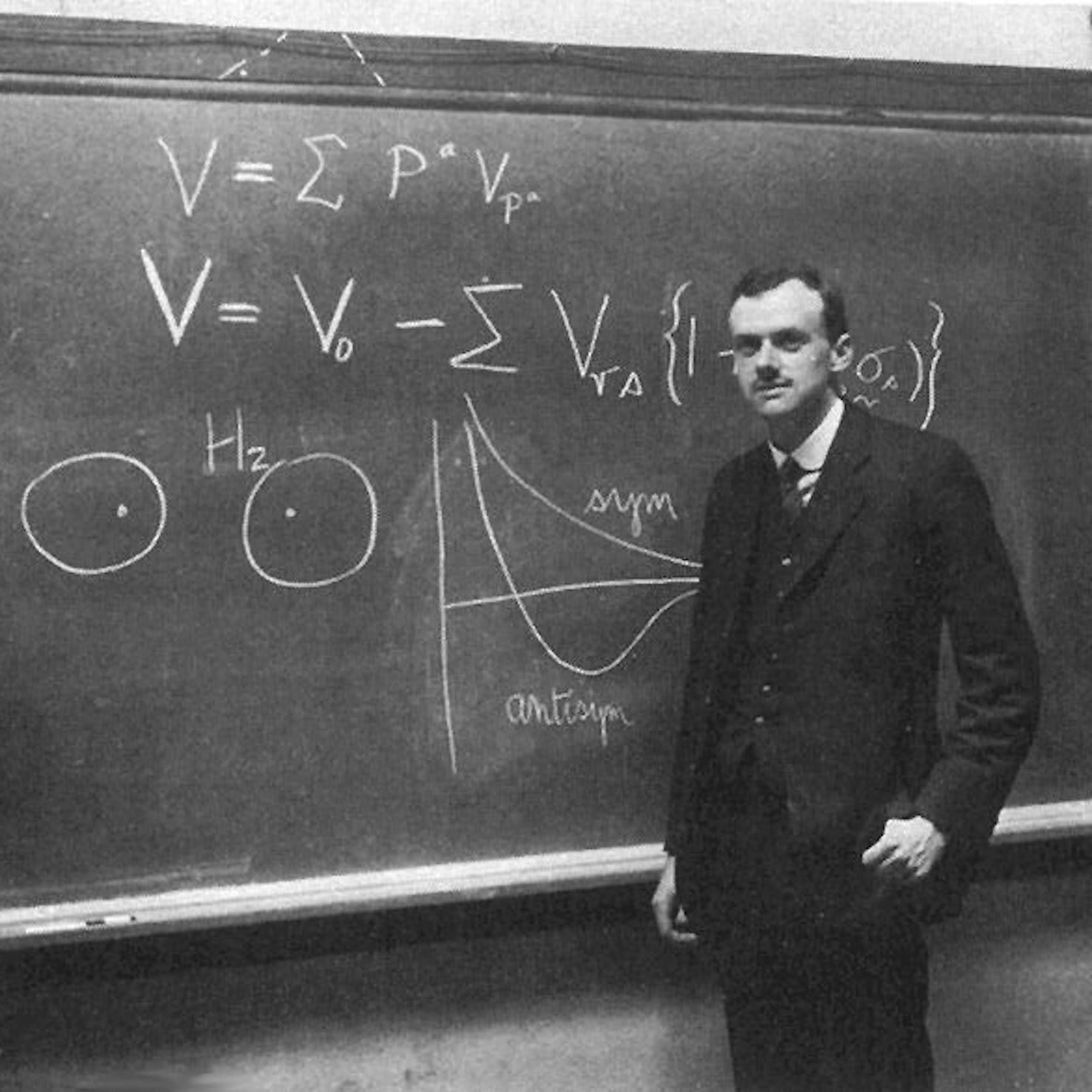 Portrait de Paul Dirac en noir et blanc, devant un tableau noir.