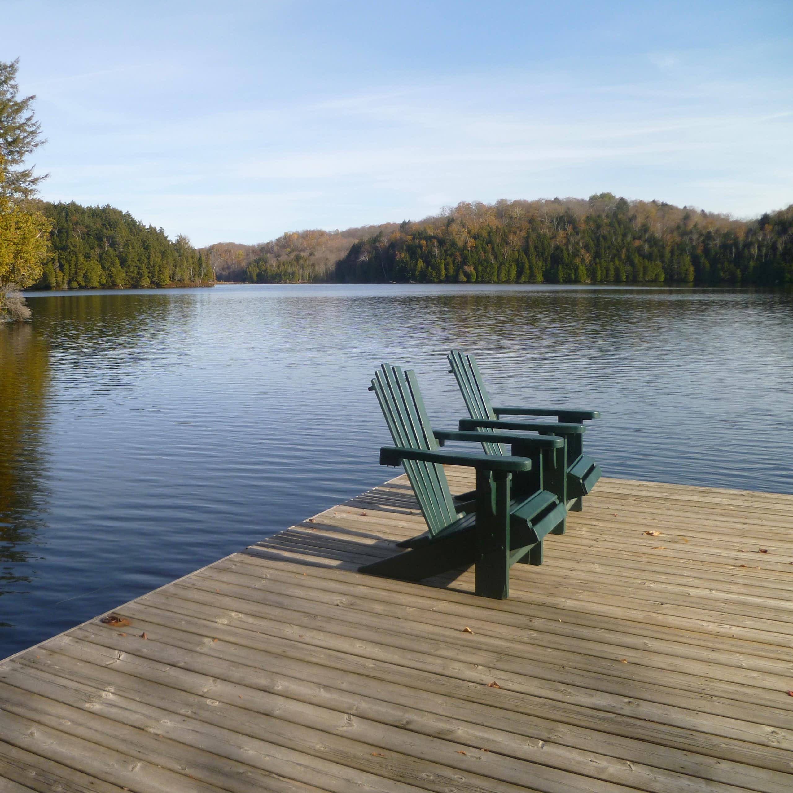 Deux chaises sont côte à côte sur le quai d'un lac entouré d'une forêt