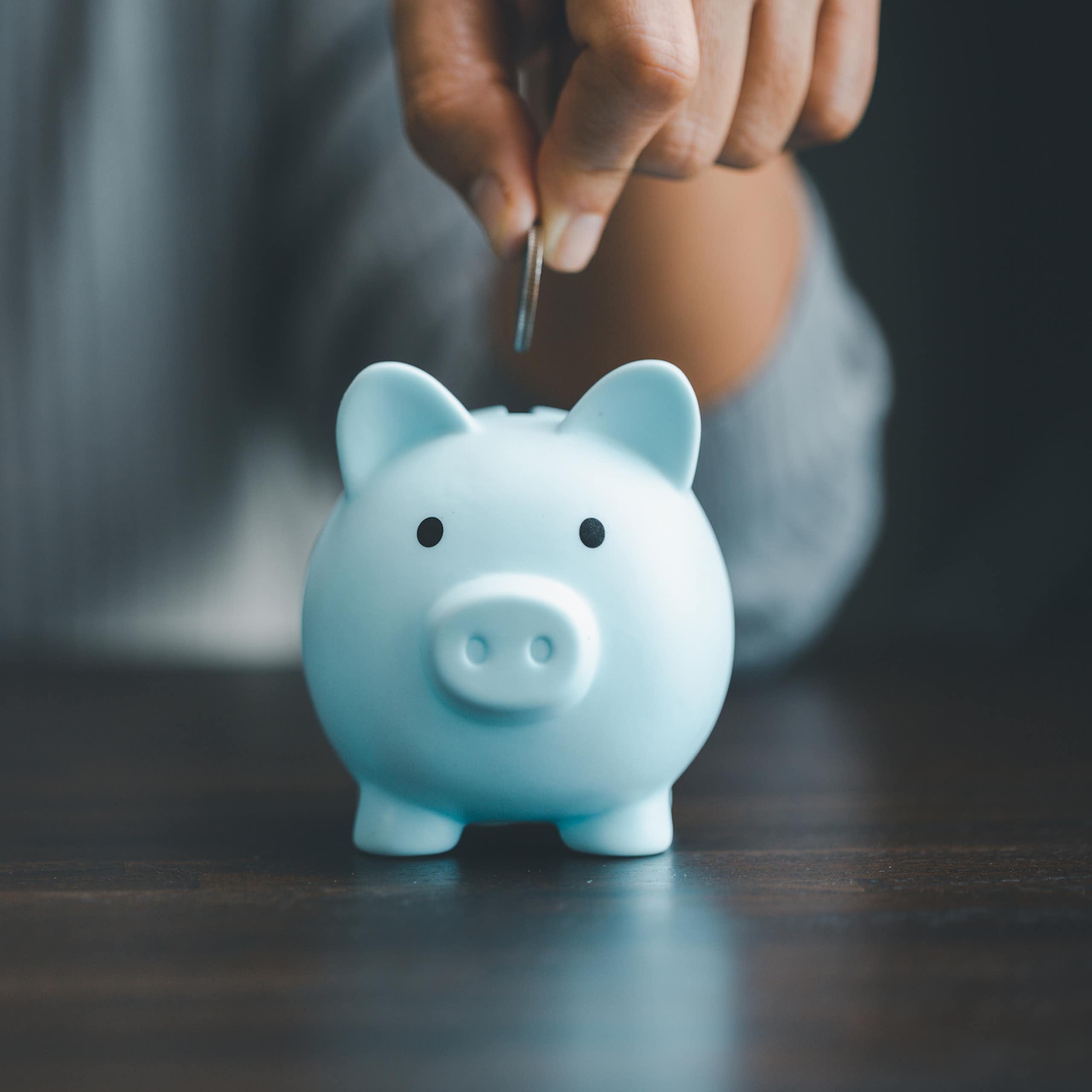 A hand dropping a coin into a piggy bank