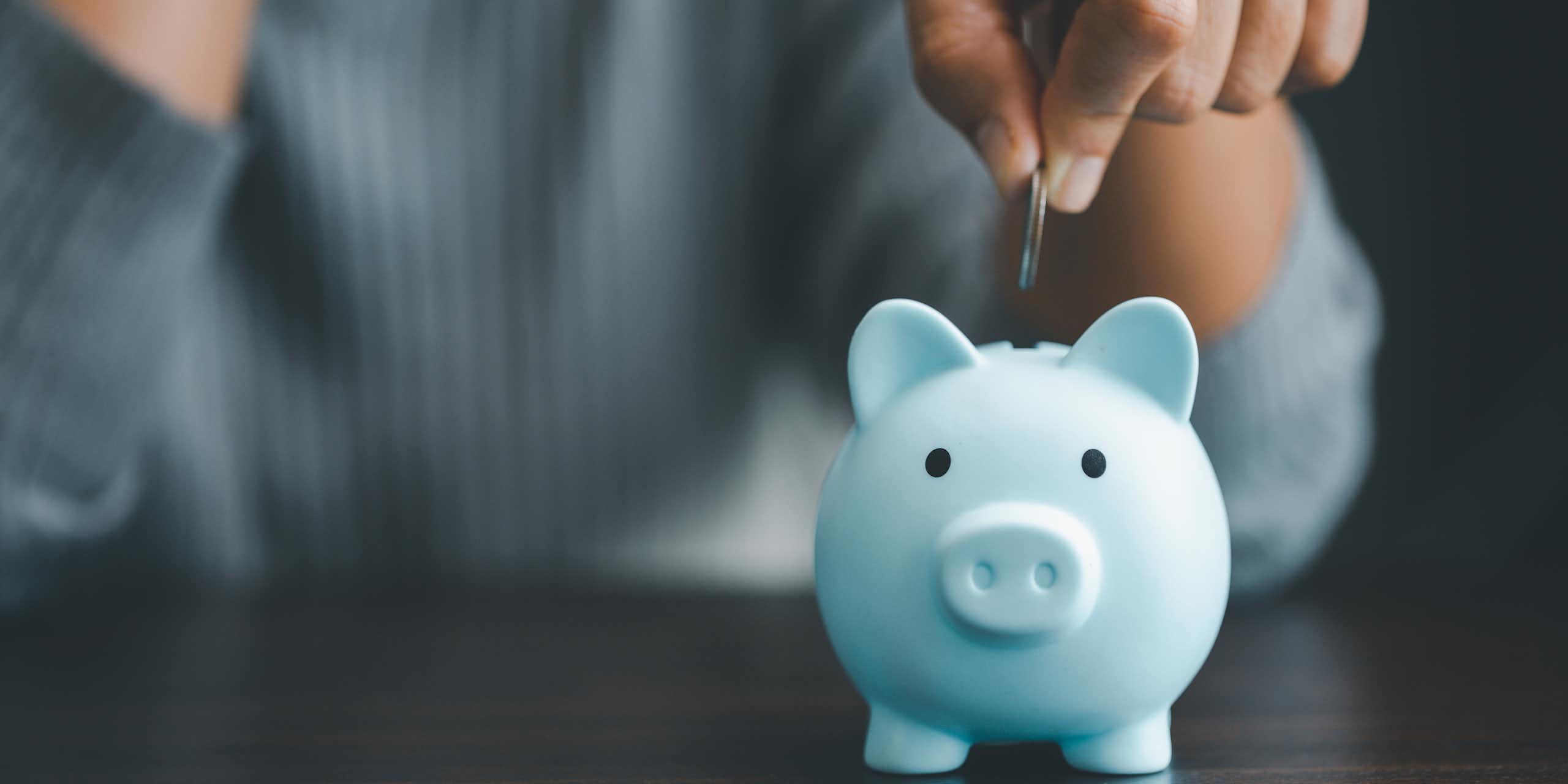 A hand dropping a coin into a piggy bank