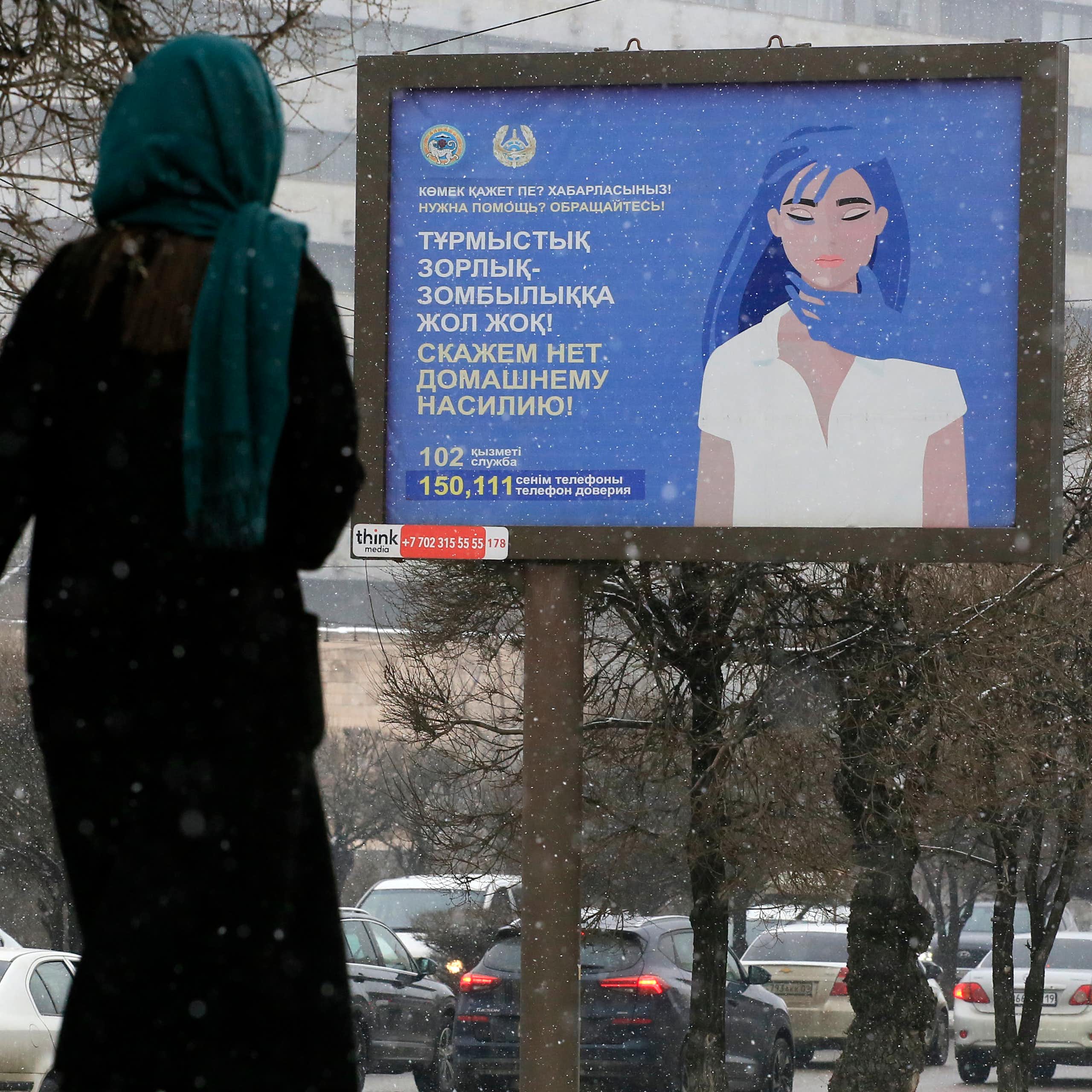 Une femme passe devant une affiche comportant des numéros de téléphone d'assistance aux victimes de violence domestique et indiquant « Dites non à la violence domestique ! » 