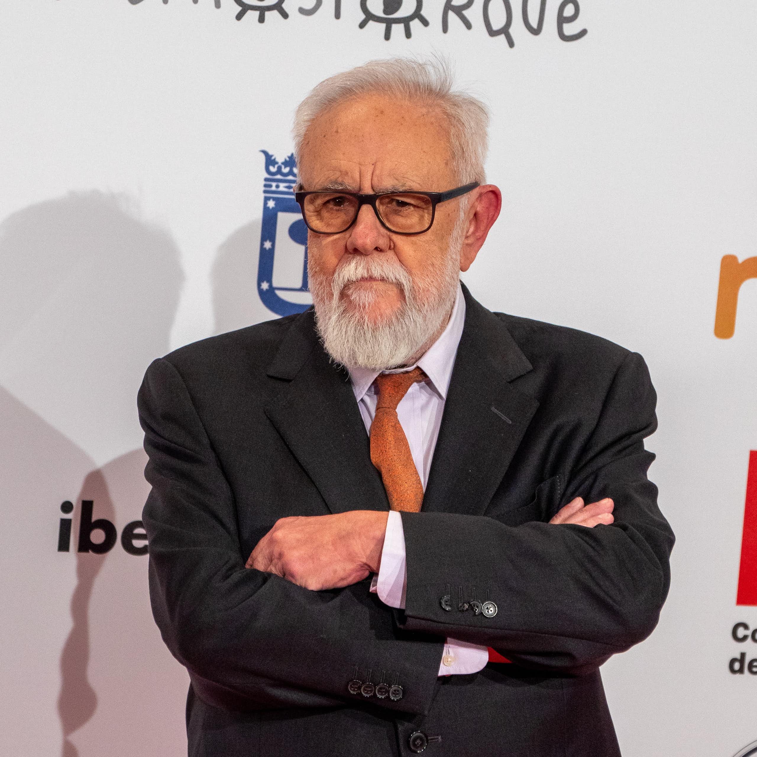 Un hombre con gafas y pelo y barba blanca, y de traje, cruza los brazos y mira a cámara.