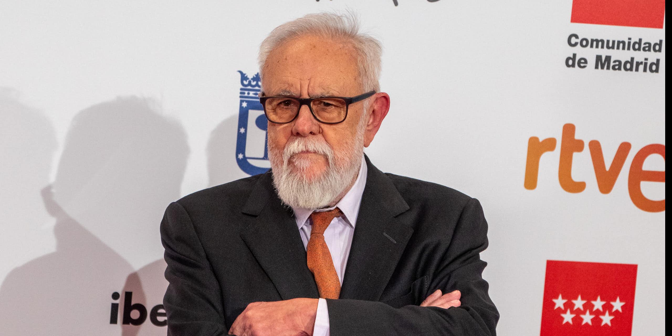 Un hombre con gafas y pelo y barba blanca, y de traje, cruza los brazos y mira a cámara.