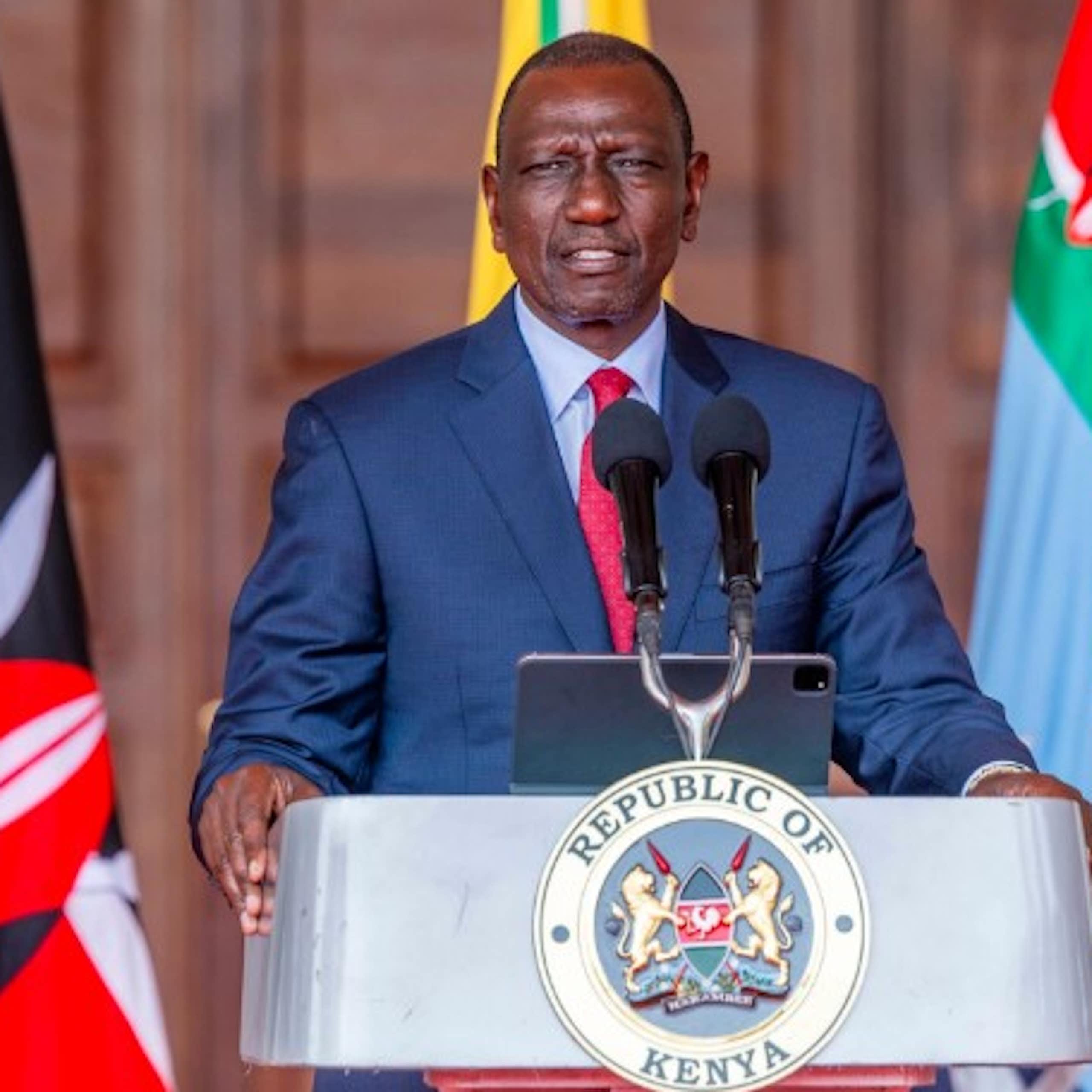 Man in suit and tie standing at a podium marked 'Republic of Kenya'