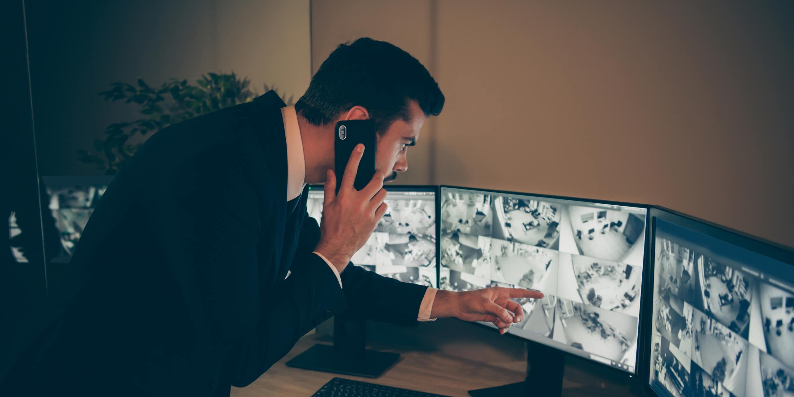 A man points at a CCTV screen while talking on a cellphone.