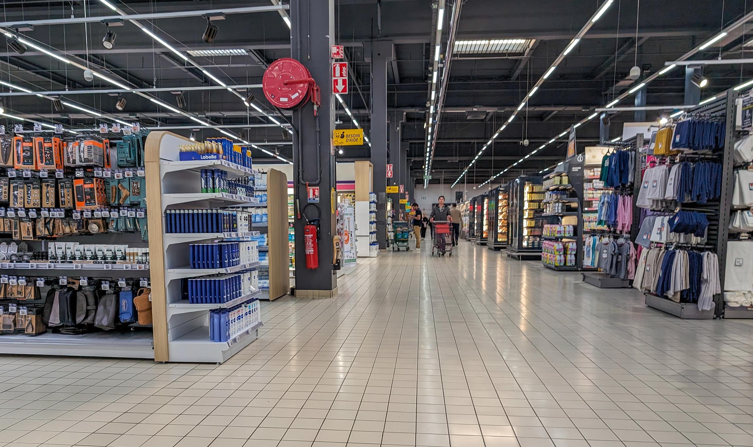 rayons d'un hypermarché avec au loin une personne qui pousse un chariot dans un magasin vide