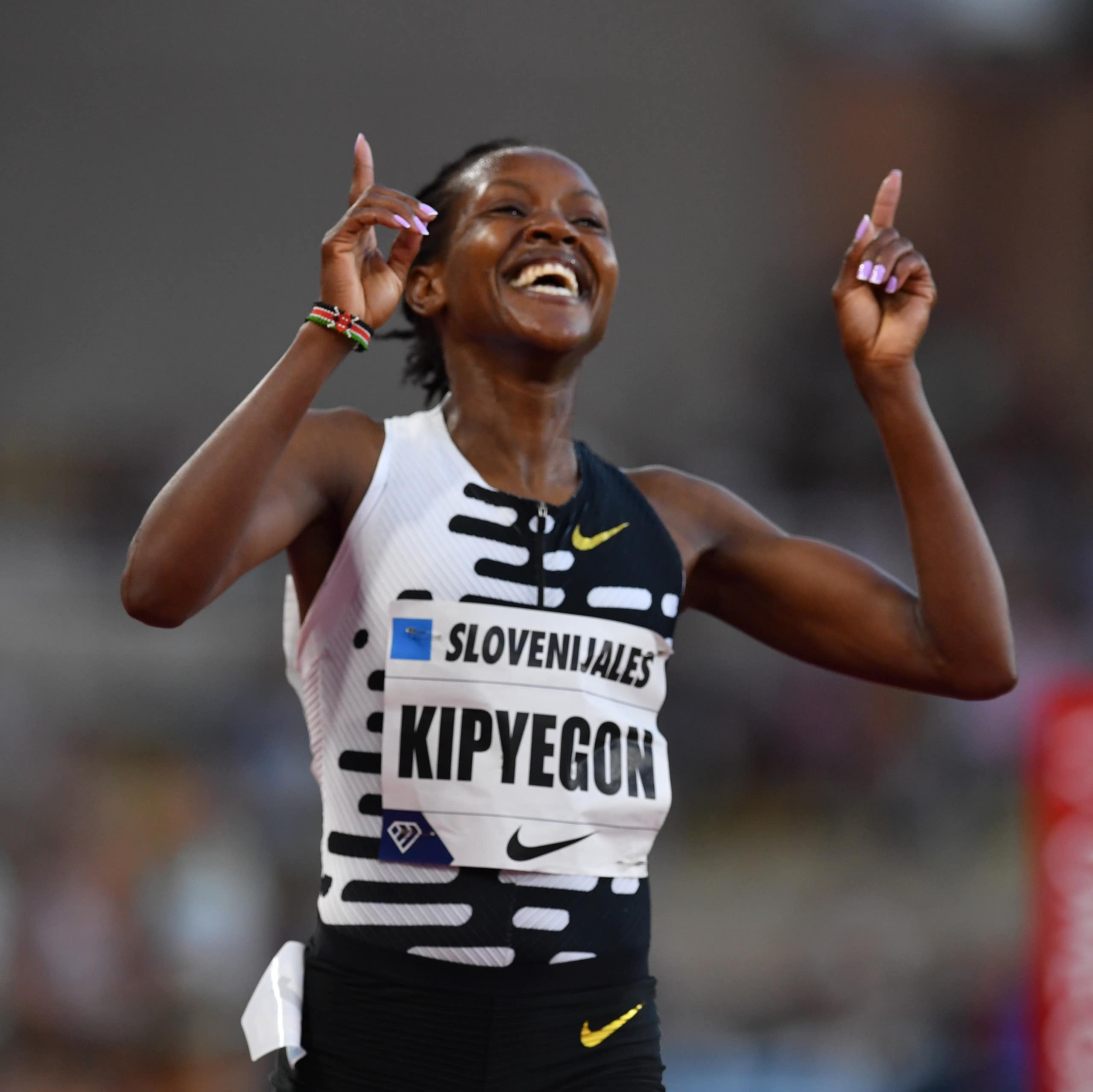 An African woman in athletics vest beams with raised arms, index fingers pointing upwards in victory.