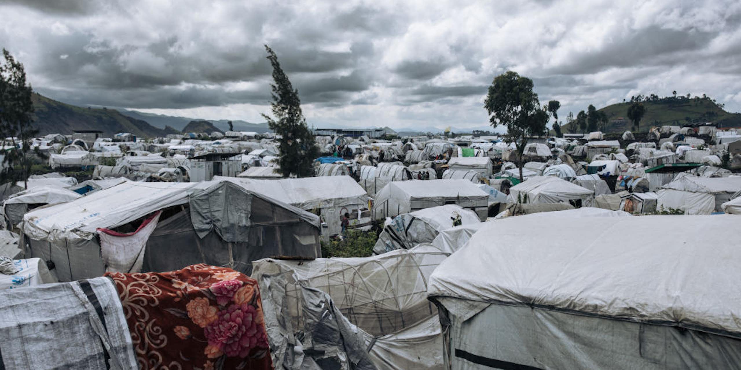 A camp of low-lying white tarpo temporary shelters of all shapes and sizes stretch back as far as the eye can see. 