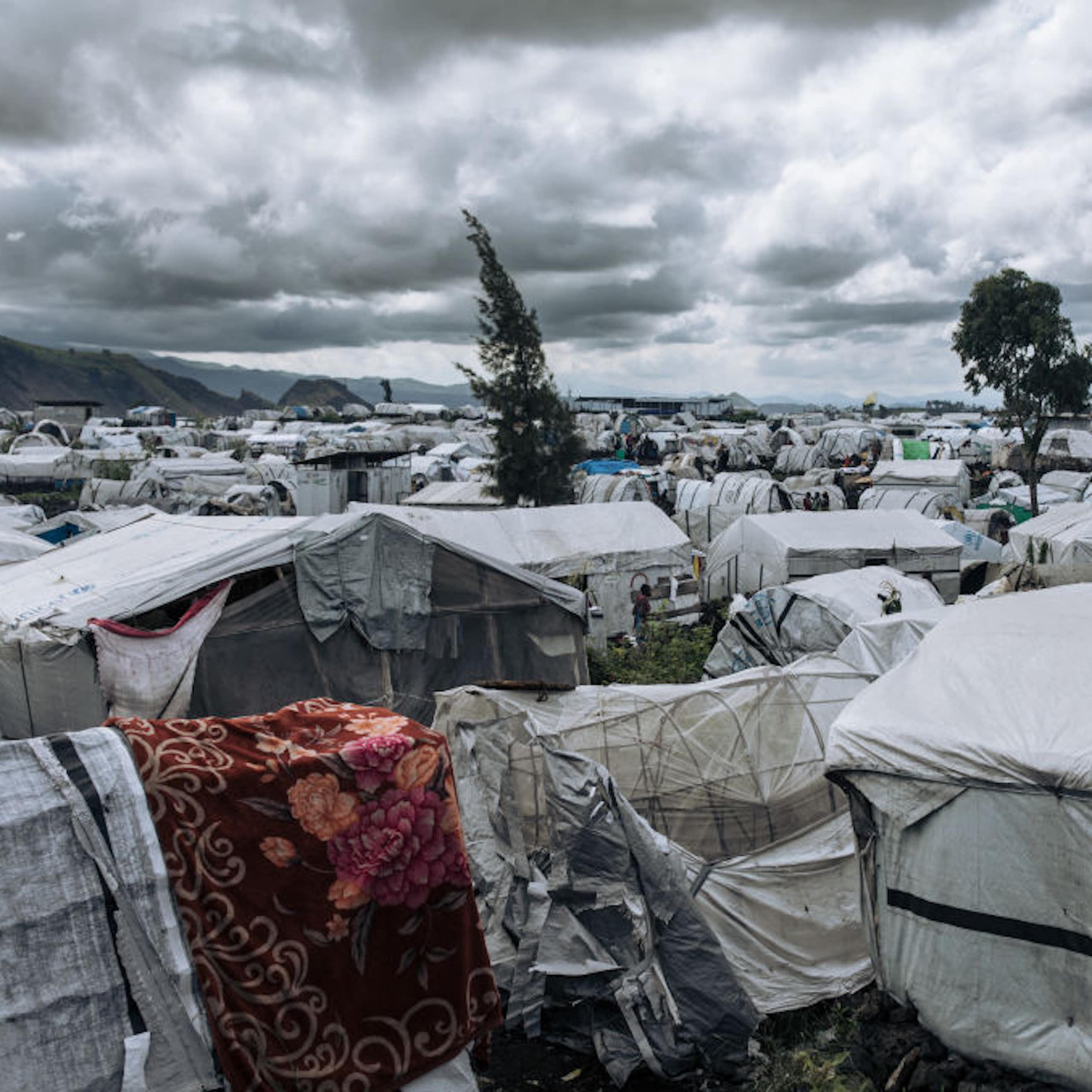 A camp of low-lying white tarpo temporary shelters of all shapes and sizes stretch back as far as the eye can see. 