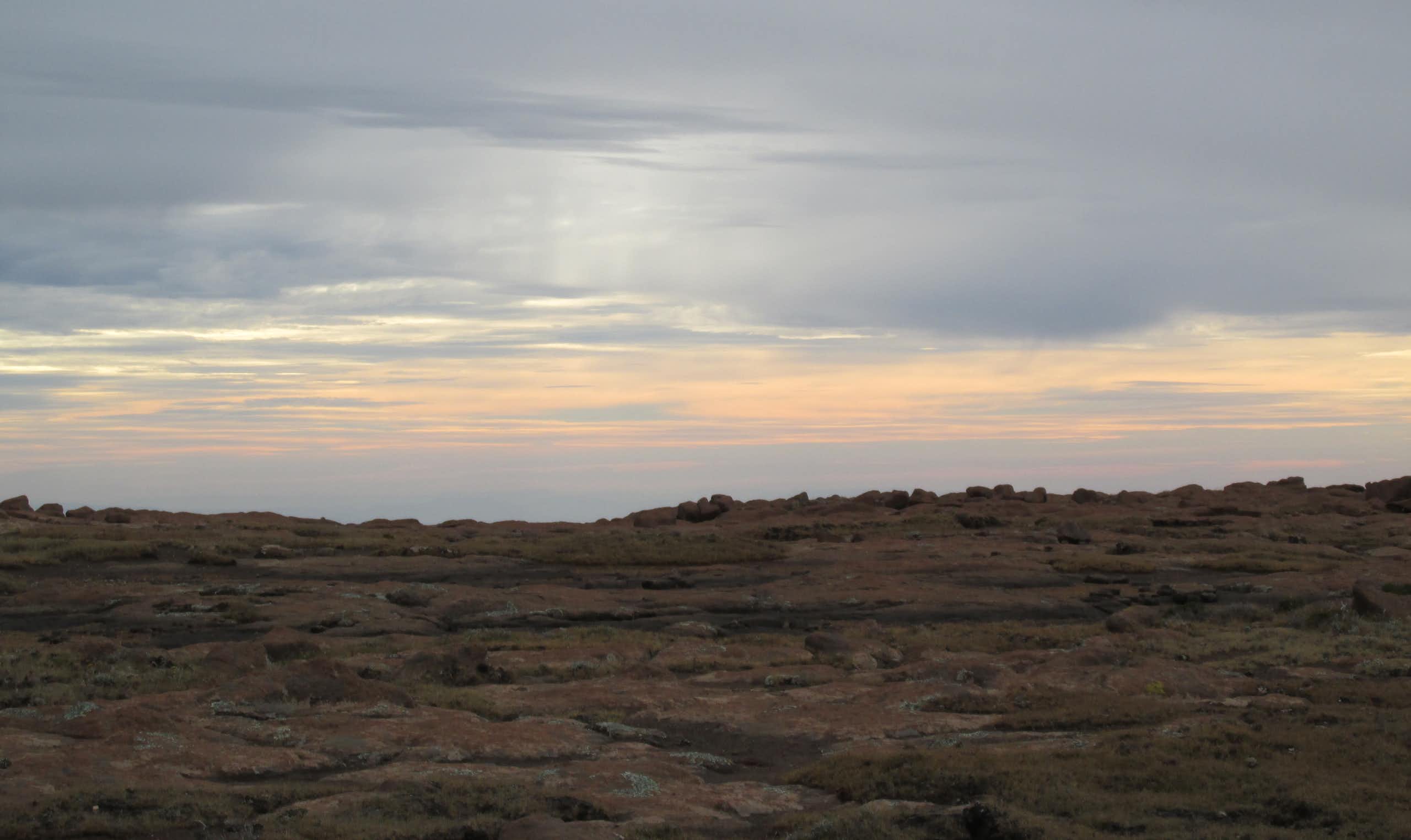 The sky, with streaks of orange and light pink on the horizon, photographed from across a rocky landscape