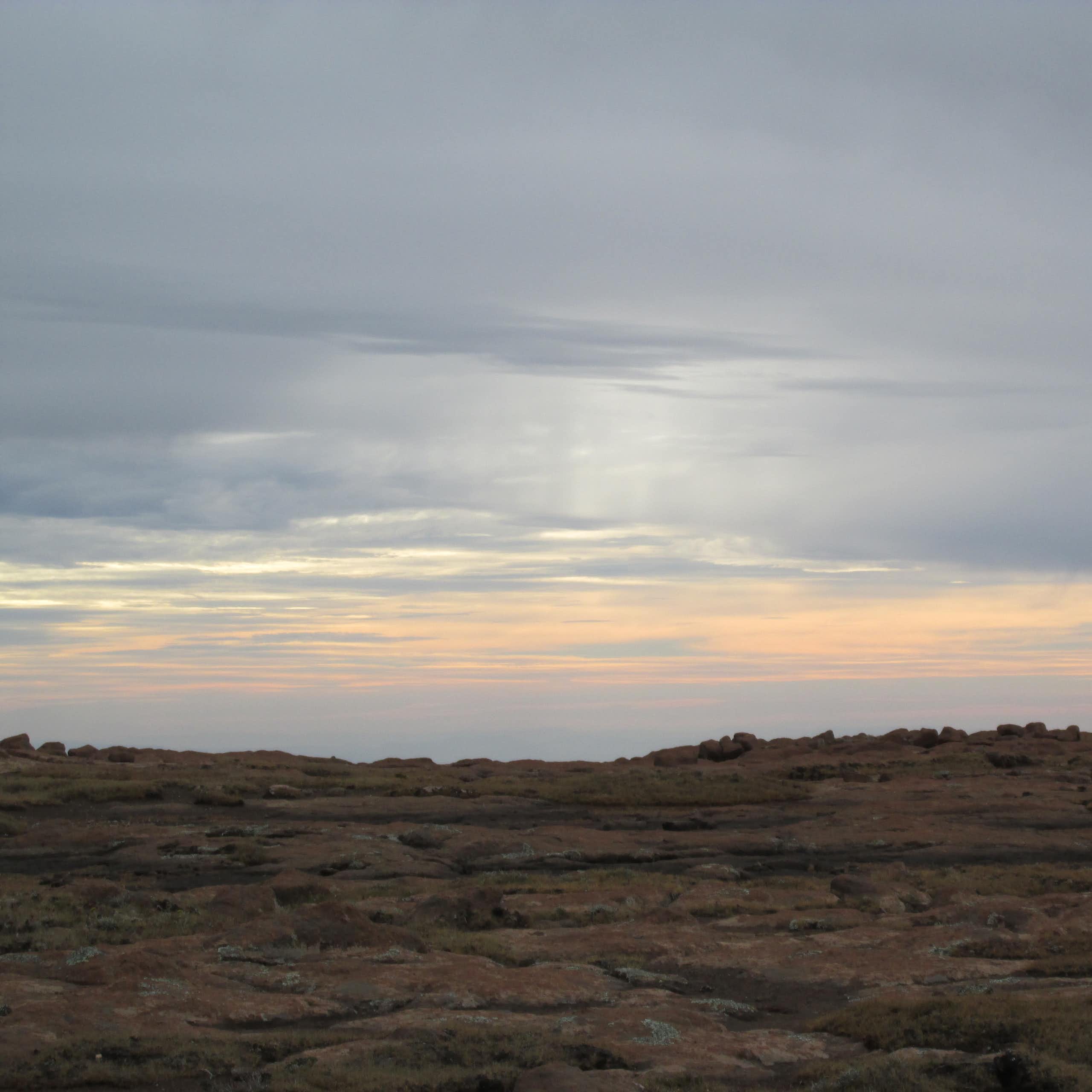 The sky, with streaks of orange and light pink on the horizon, photographed from across a rocky landscape