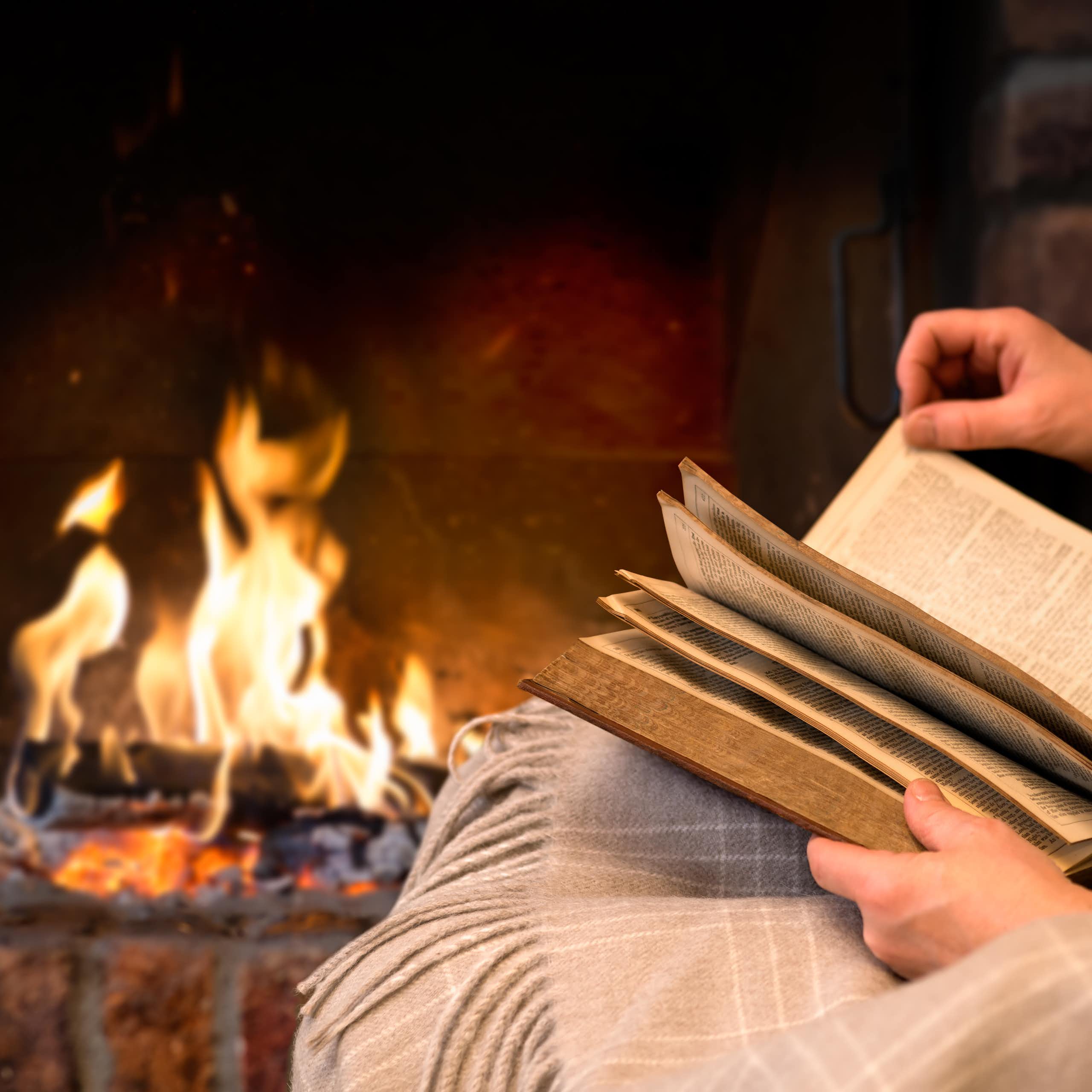 A person reads a book in front of an open fireplace