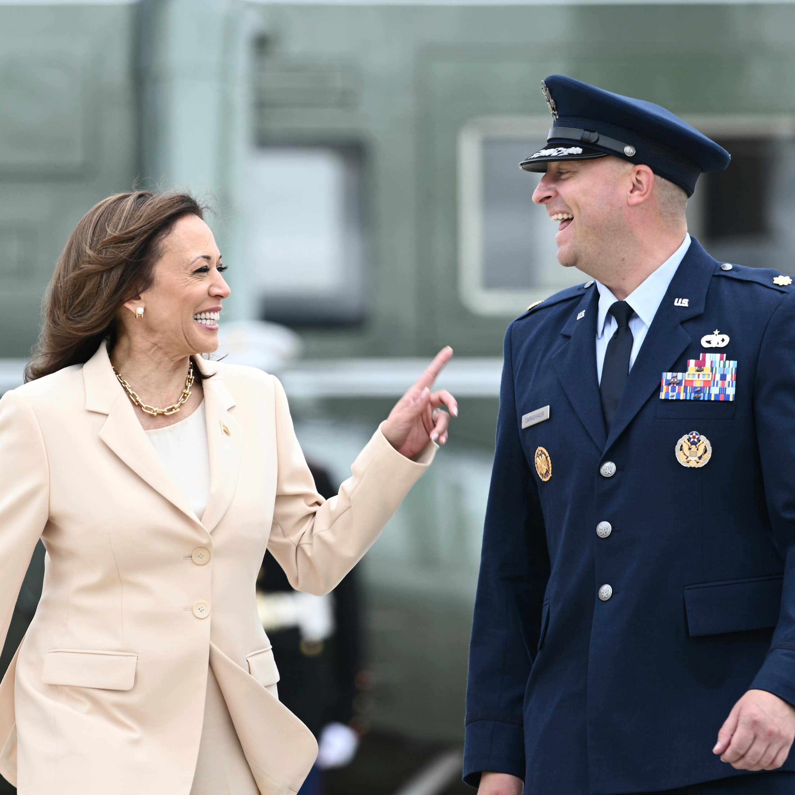 A woman with dark hair in a cream suit laughs with a man in an Air Force uniform.