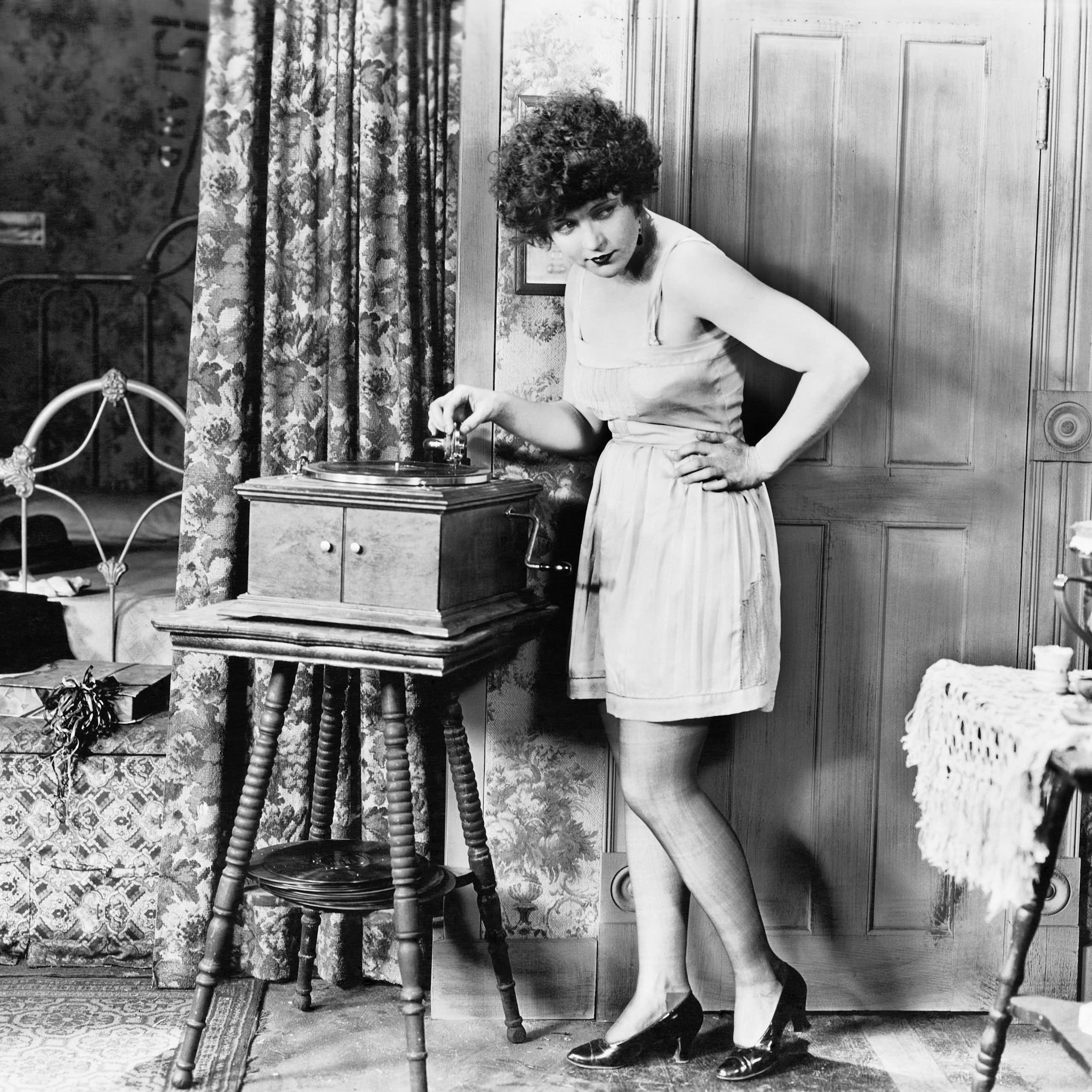 Una foto en blanco y negro de una mujer a punto de poner un disco en un reproductor antiguo.