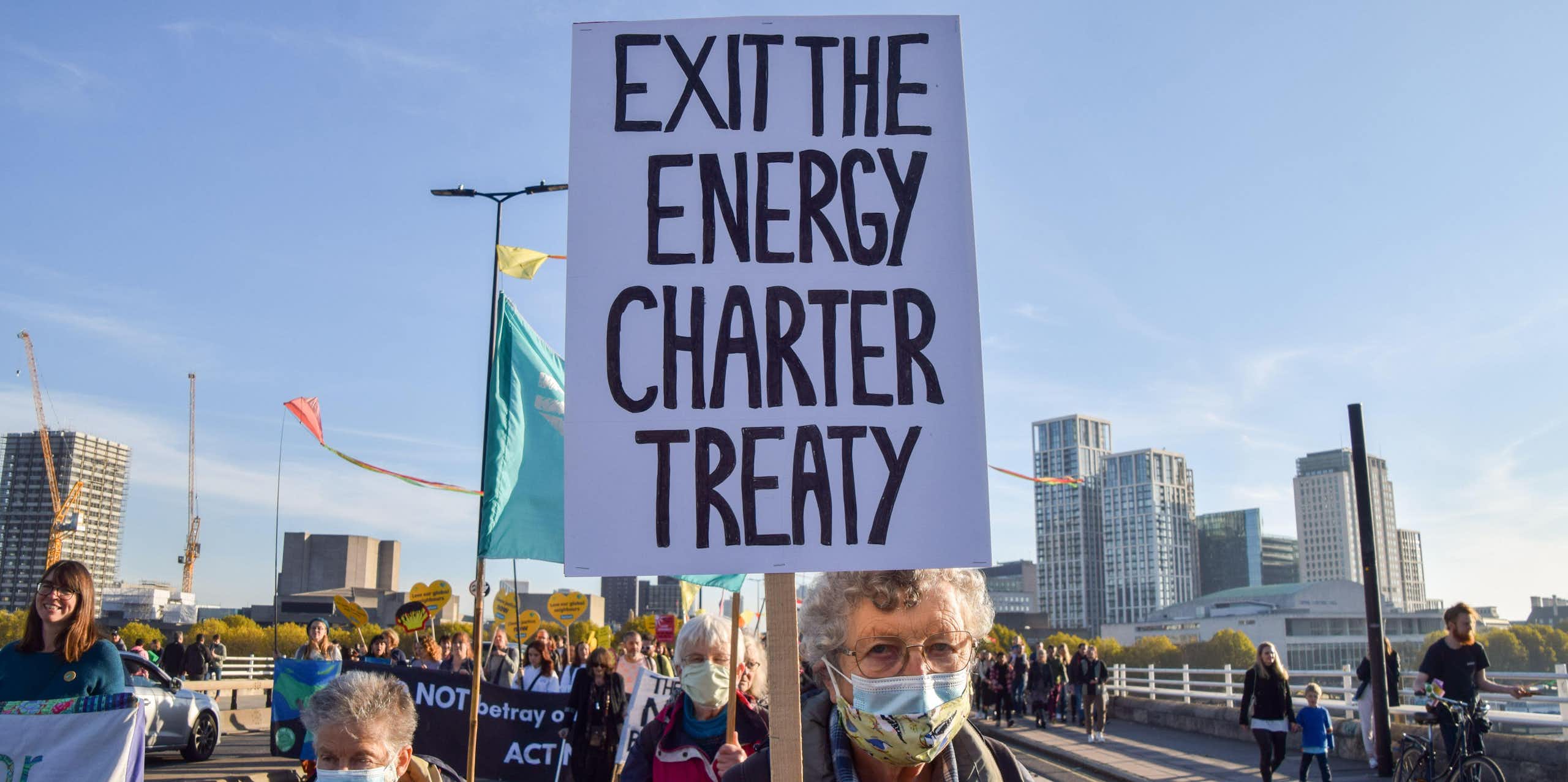 A woman holds up a sign that says Exit the Energy Charter Treaty. 