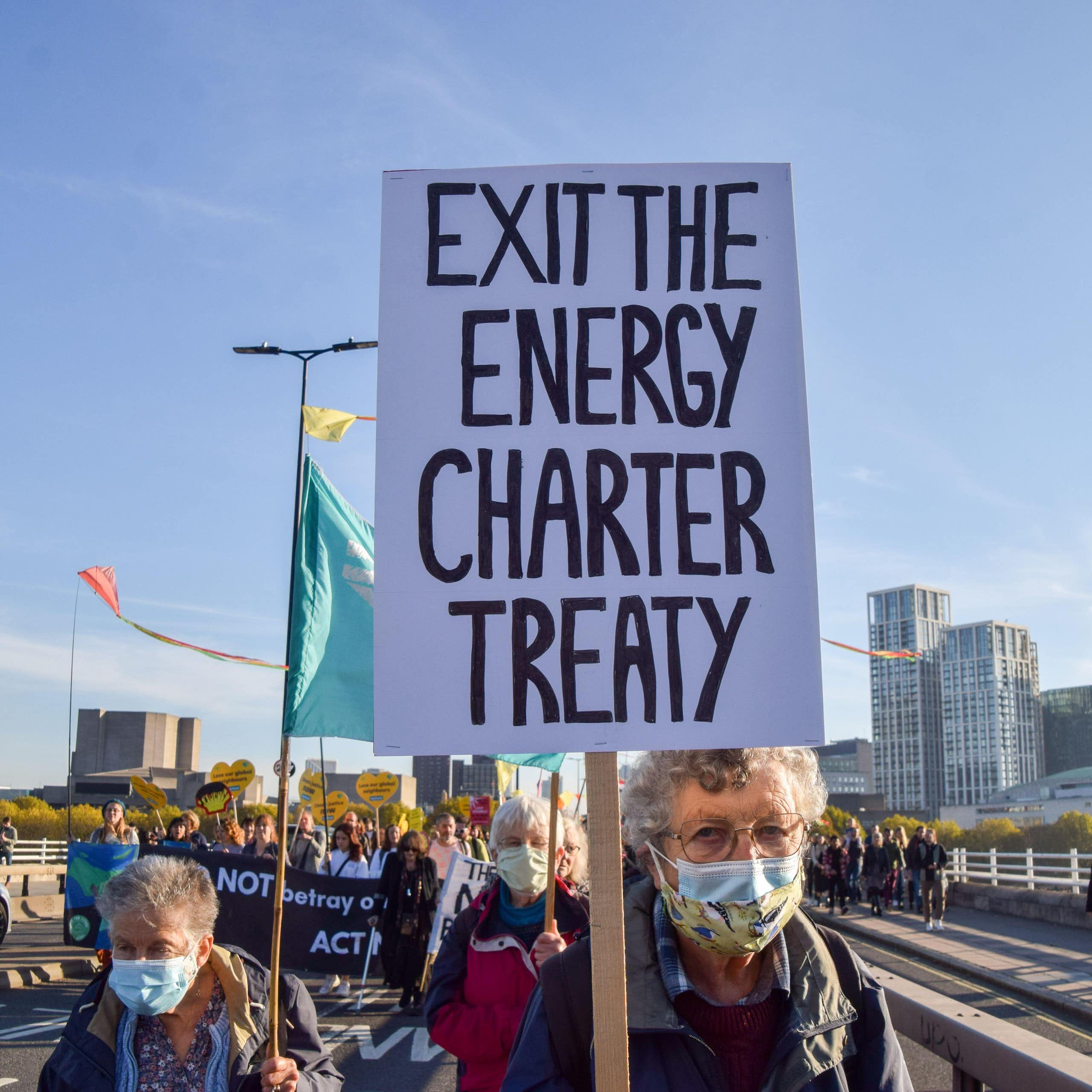 A woman holds up a sign that says Exit the Energy Charter Treaty. 