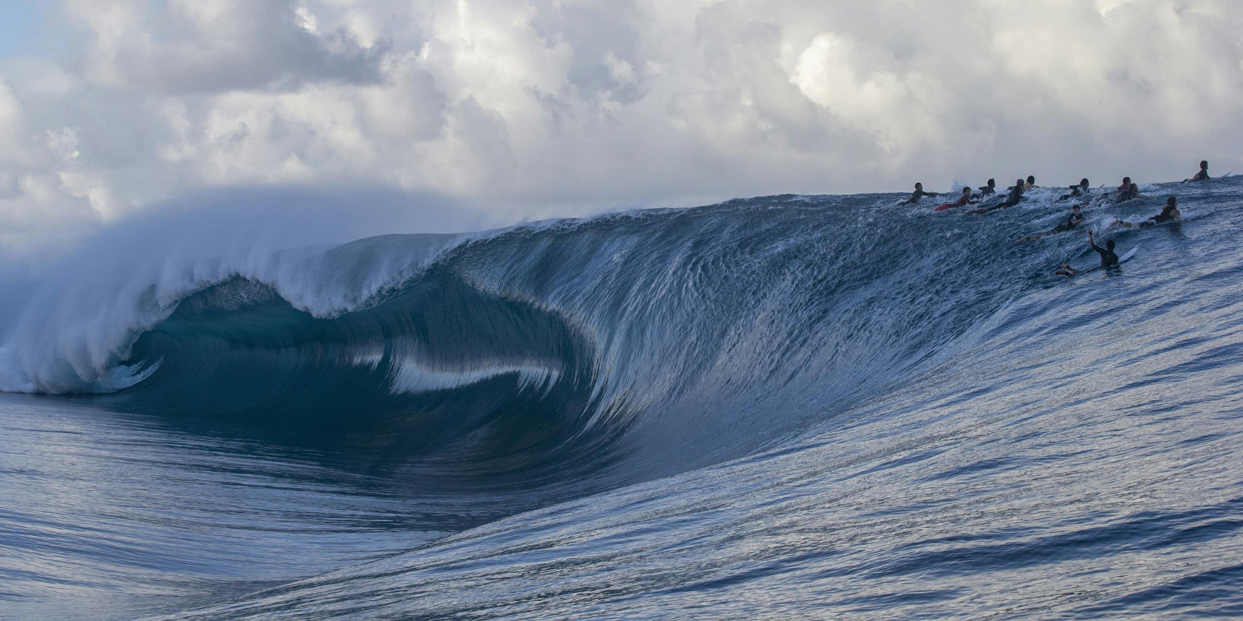 Surfers cresting breaking wave at Teahupo'o