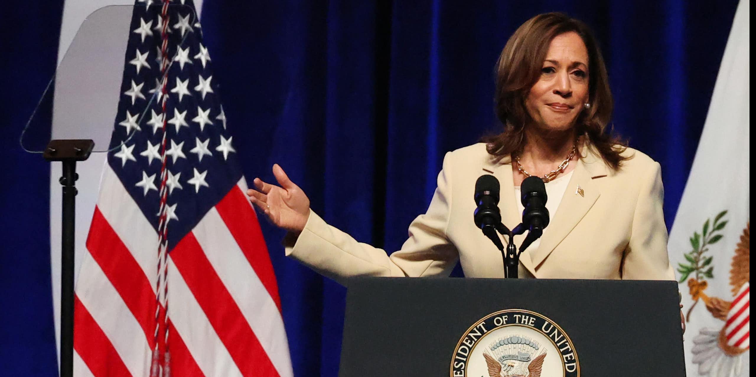 US vice-president Kamala Harris stadns at a podium gesturing towards an American flag.
