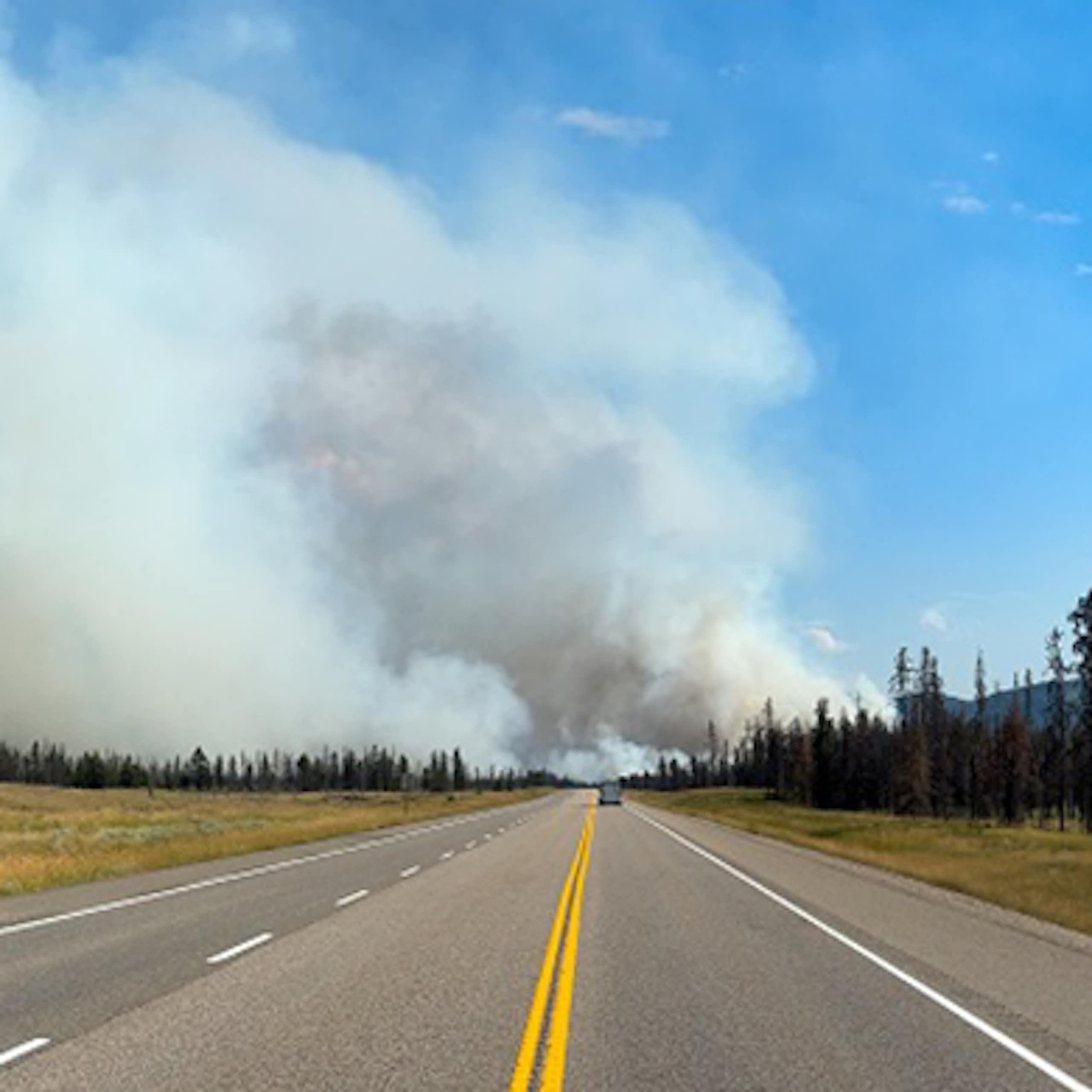Wildfire smoke is seen down a road next to a mountain range.