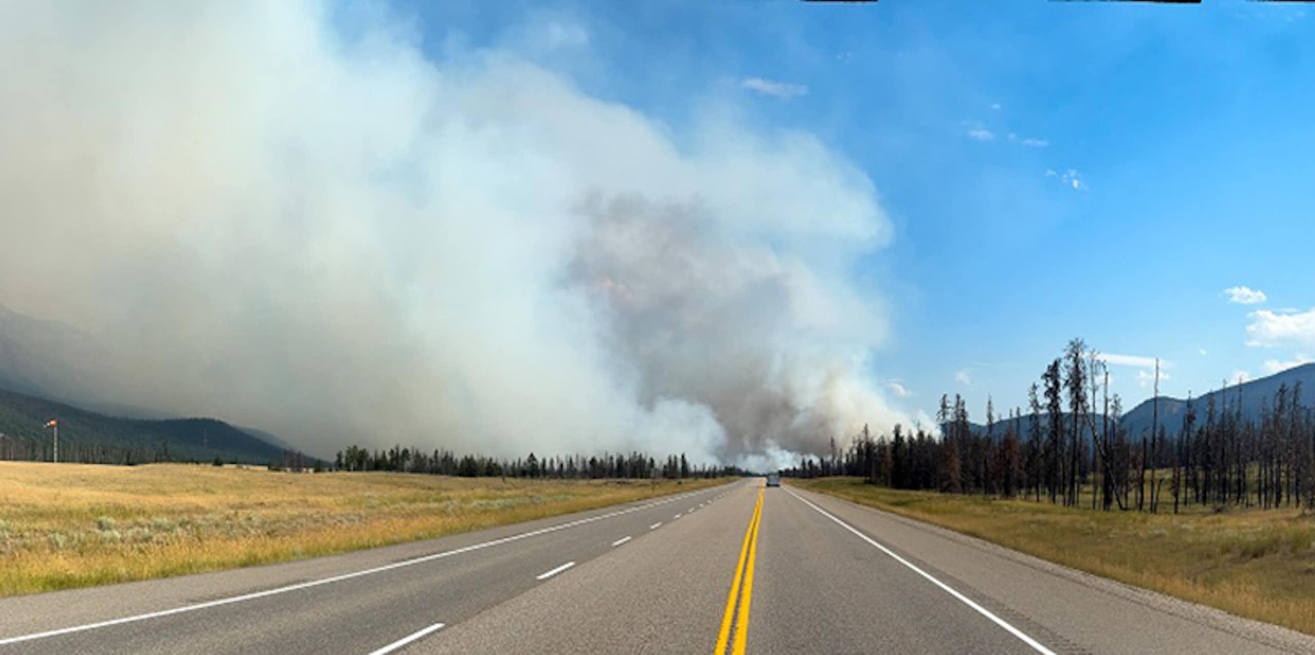 Wildfire smoke is seen down a road next to a mountain range.