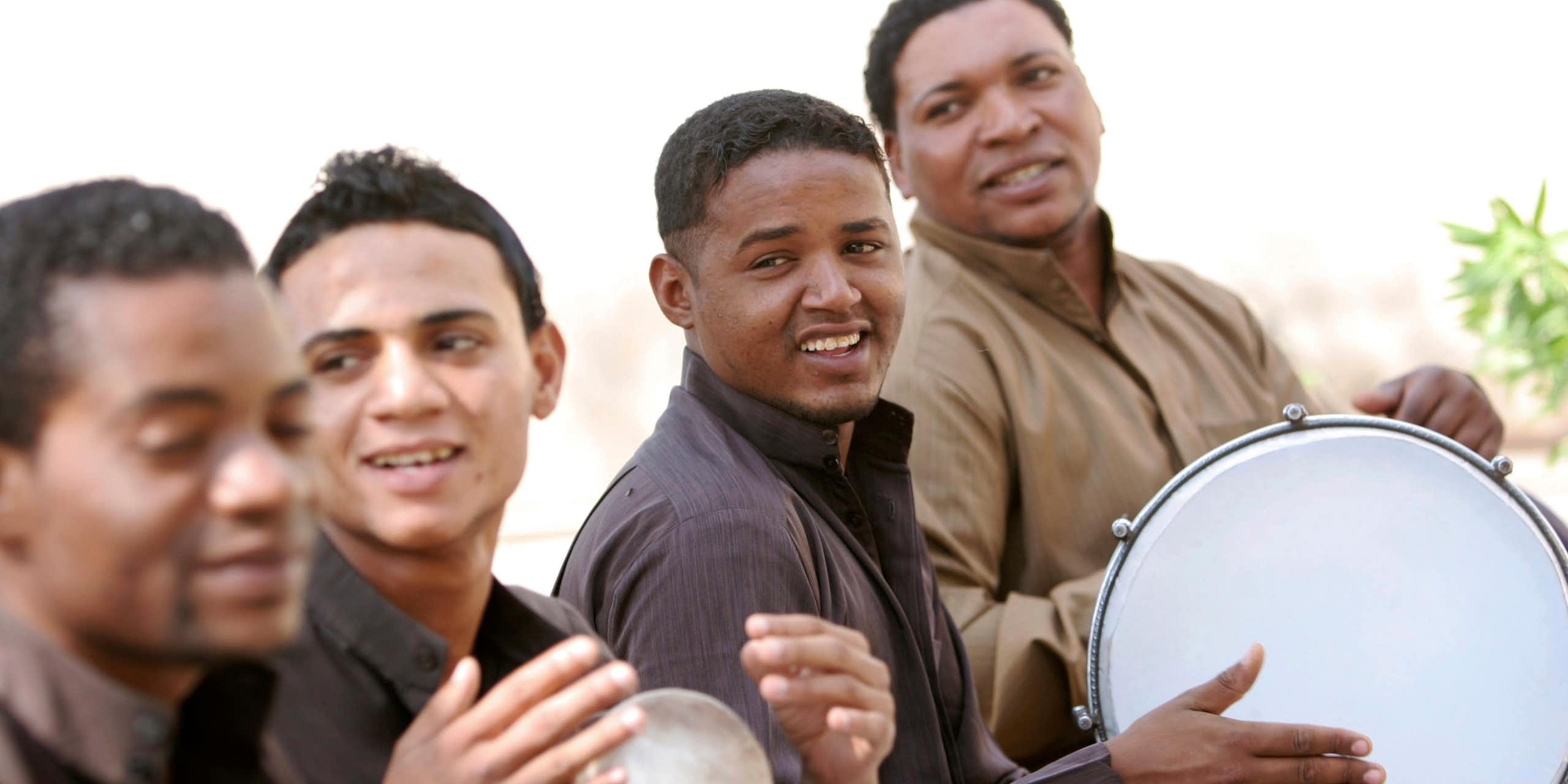Men sit in a row playing drums