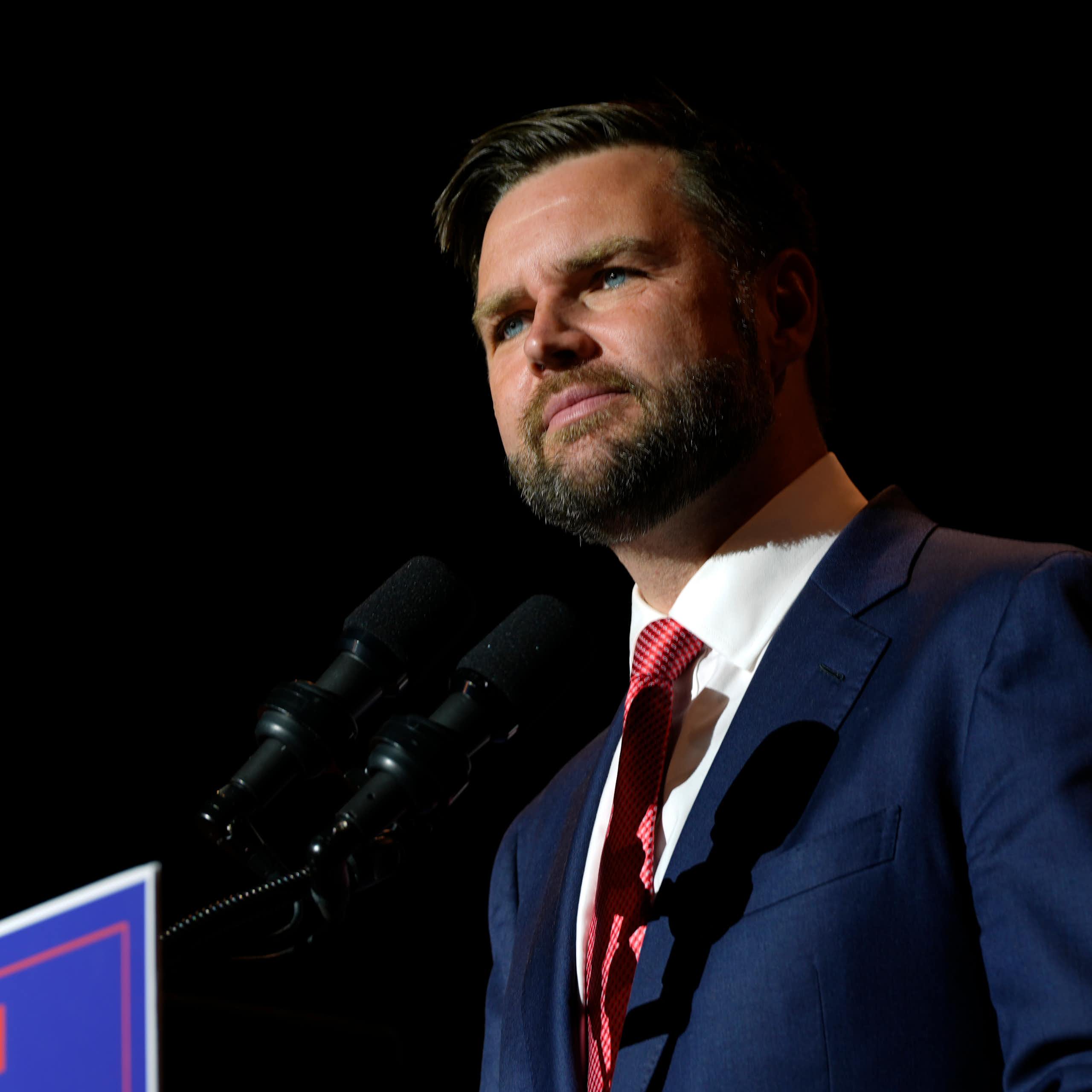 A middle-aged white man stands before a podium with a microphone on it